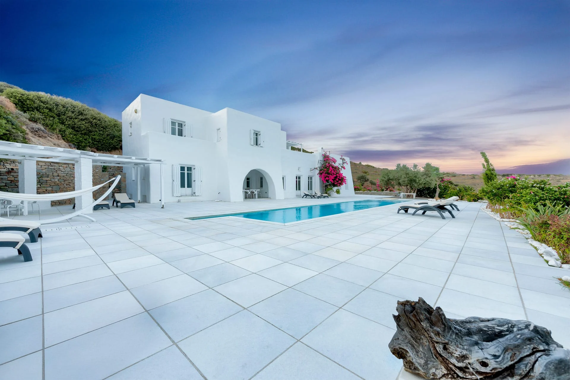White villa and swimming pool on a paved terrace at dusk in Paros, Greece