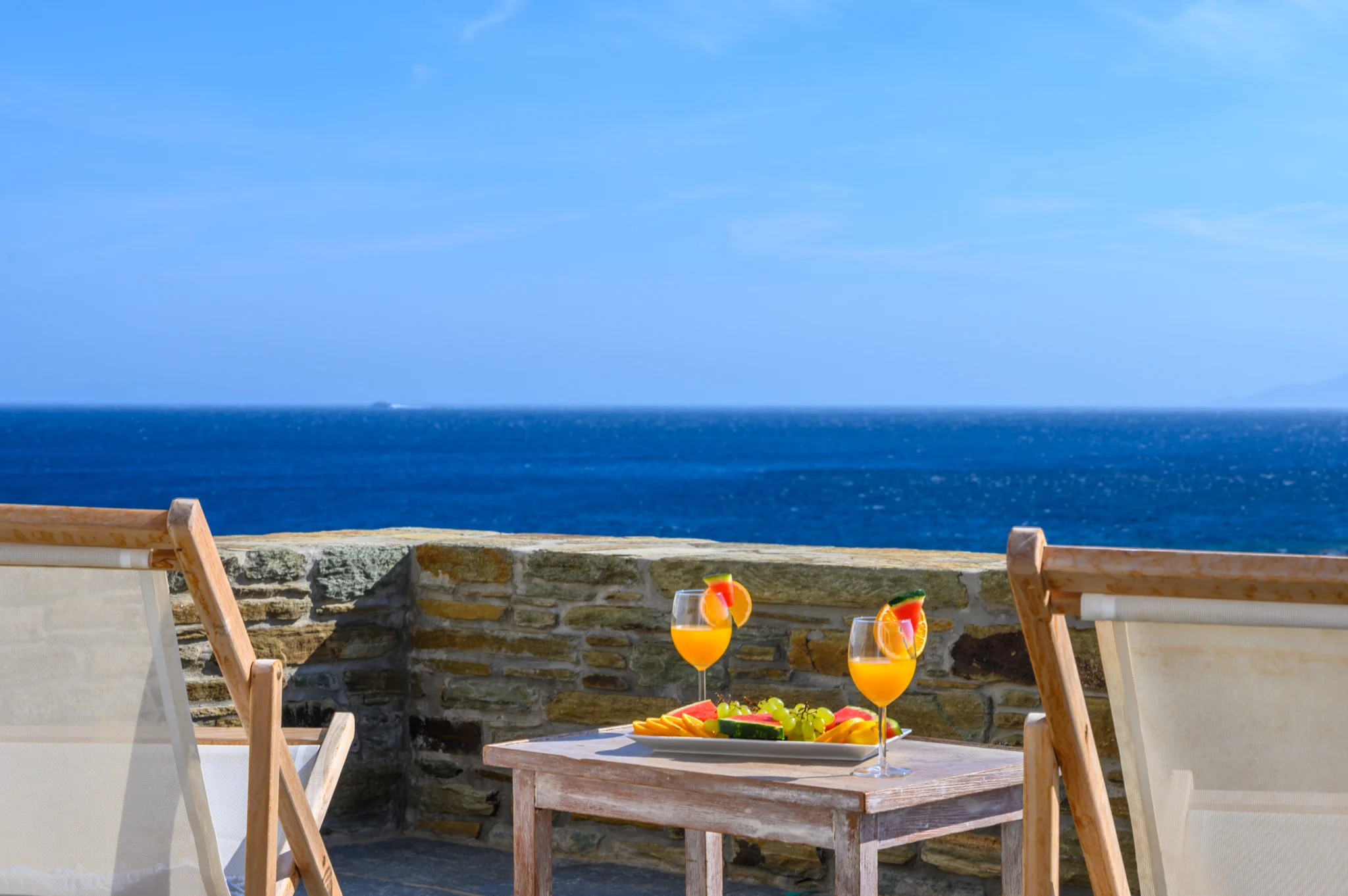 Villa Golden Beach — Sea-view terrace, Andros Timber terrace chairs with fruit and drinks overlooking the blue sea at Villa Golden Beach in Andros