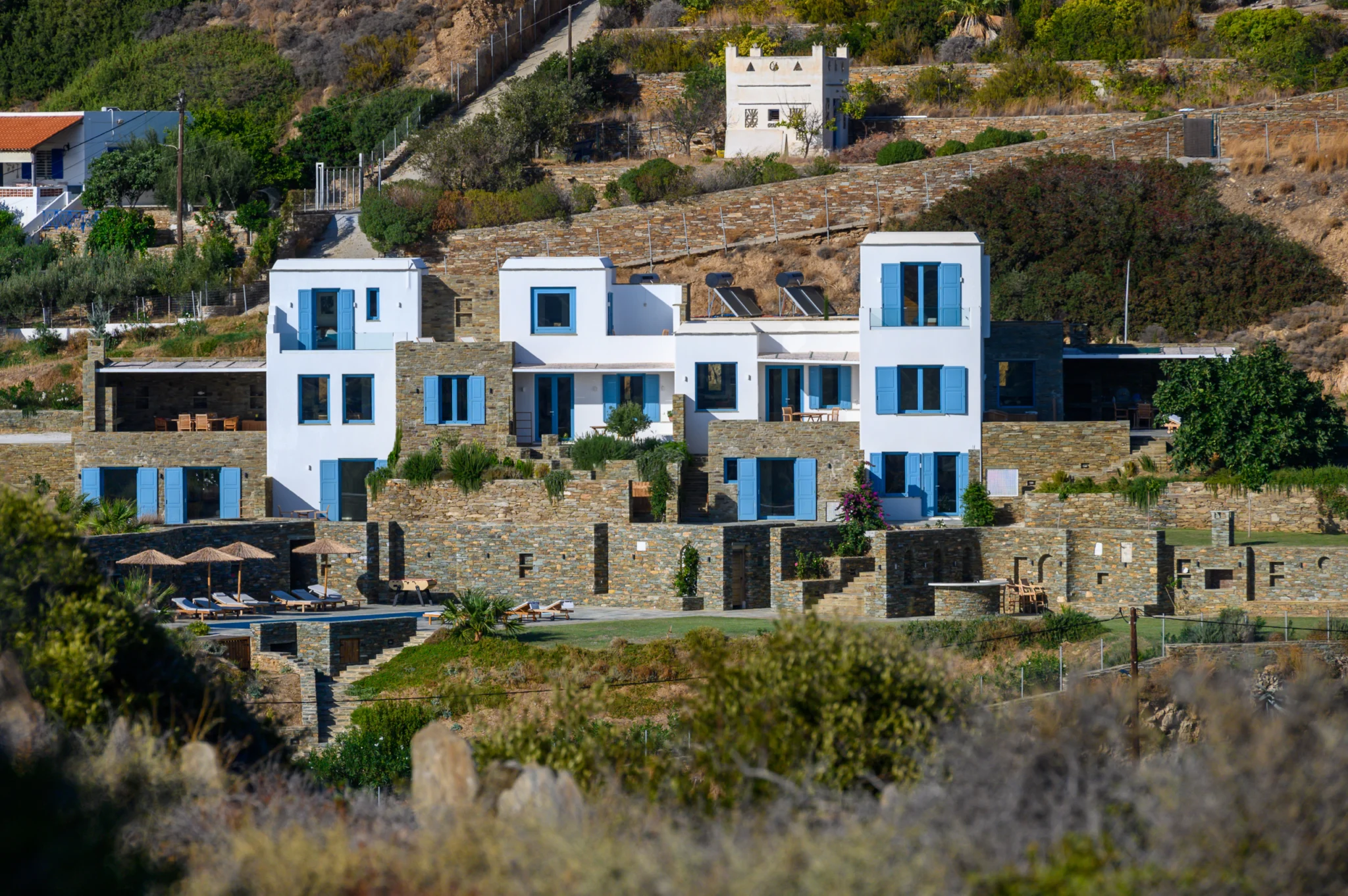 Villa Golden Beach — Villa in the landscape, Andros White villa buildings with blue shutters and stone terraces on the hillside at Villa Golden Beach in Andros