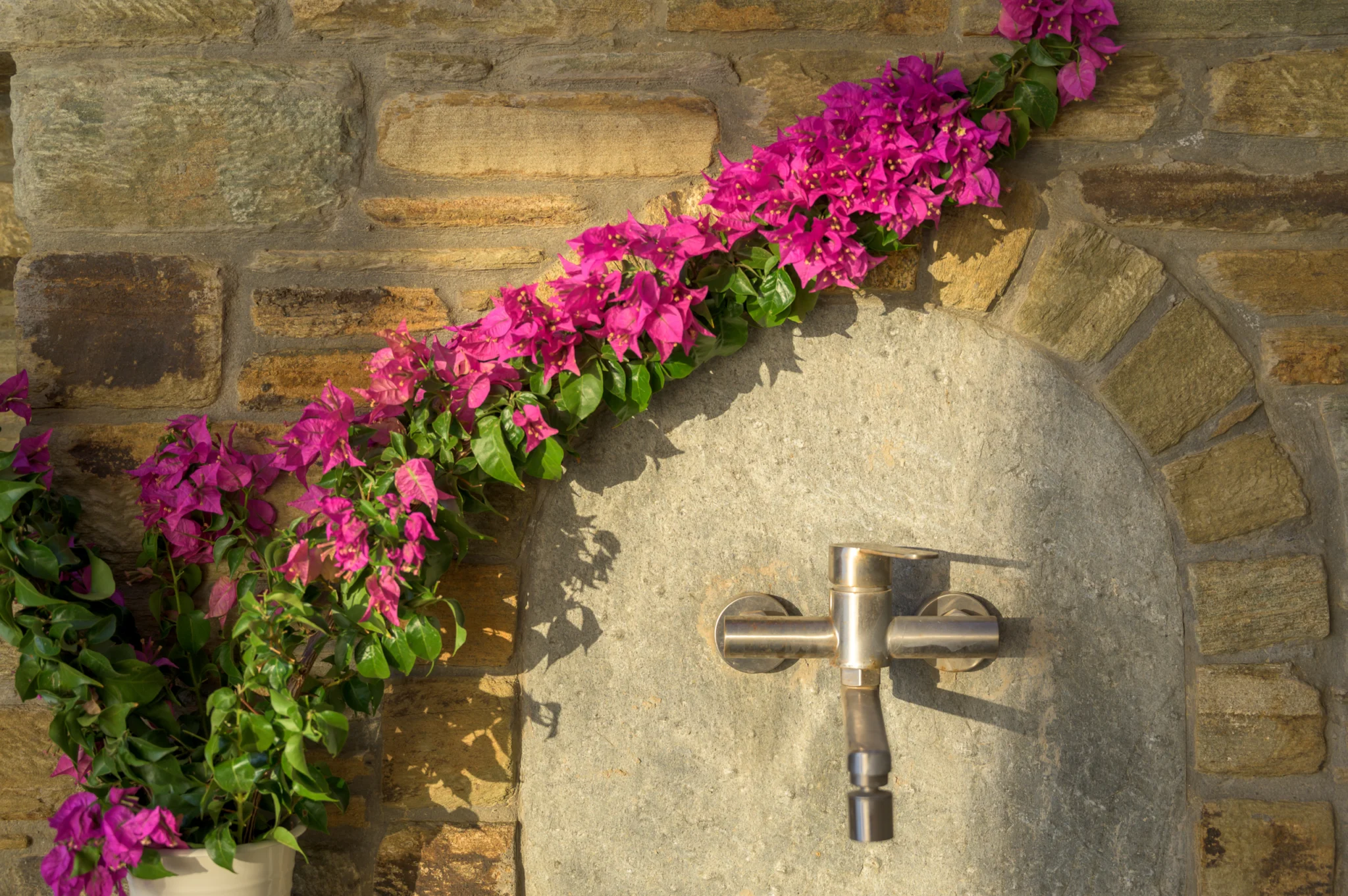 Villa Golden Beach — Stone fountain detail, Andros Metal tap in an arched stone recess decorated with pink bougainvillea at Villa Golden Beach in Andros
