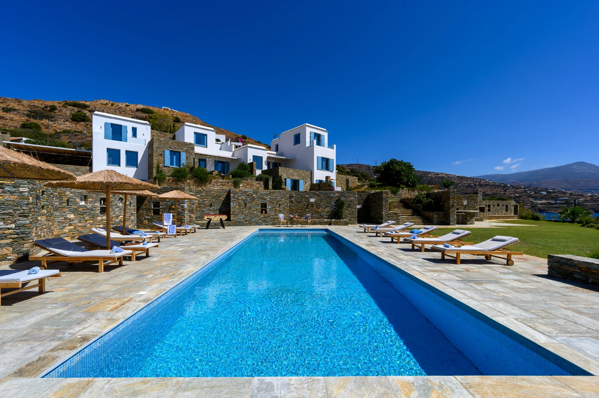 Villa Golden Beach — Swimming pool in daylight, Andros Long blue swimming pool with sun loungers and white villa buildings at Villa Golden Beach in Andros