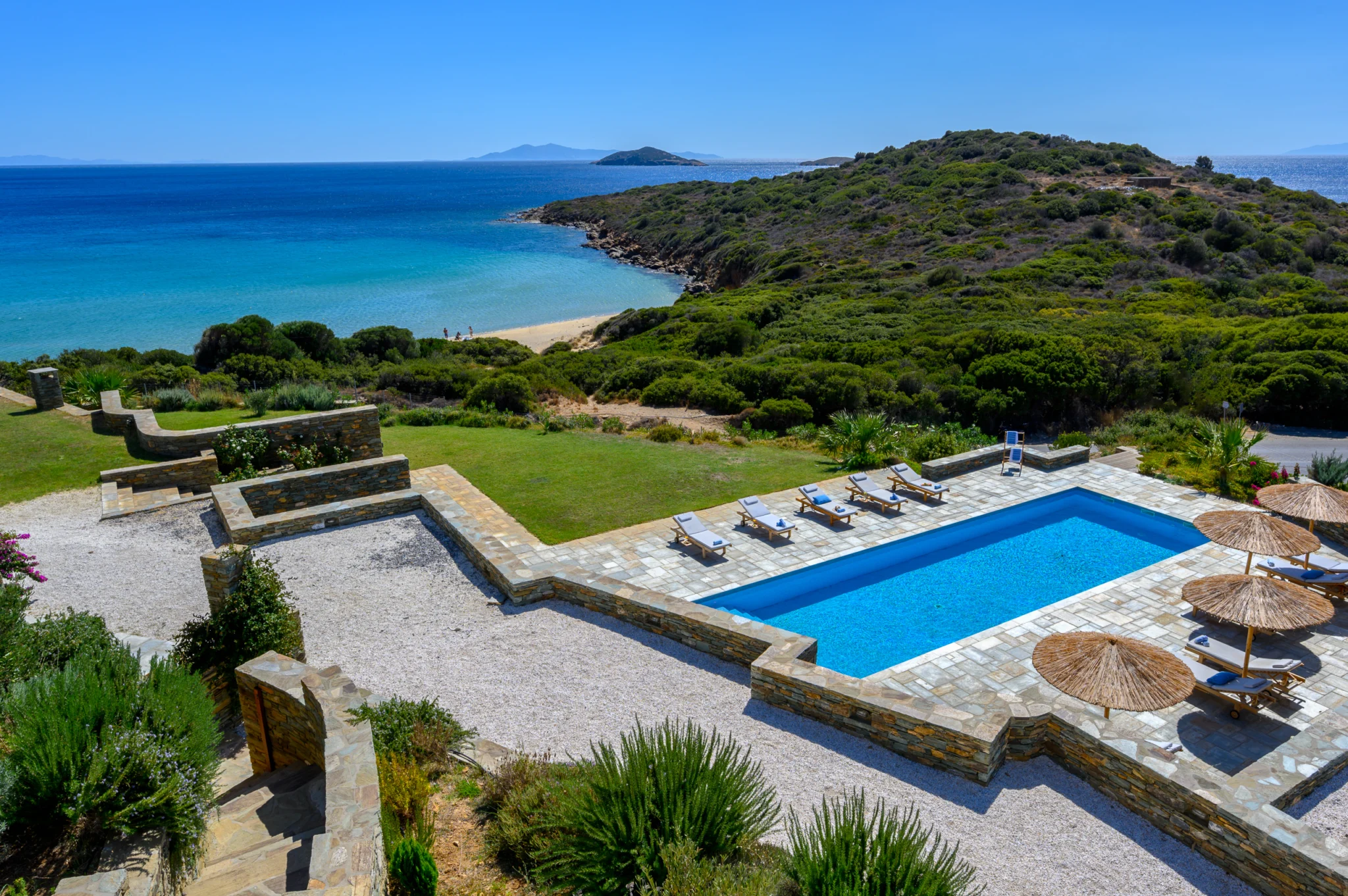 Villa Golden Beach — Pool and coastal setting, Andros Elevated view of the swimming pool and sun terraces overlooking a turquoise bay at Villa Golden Beach in Andros