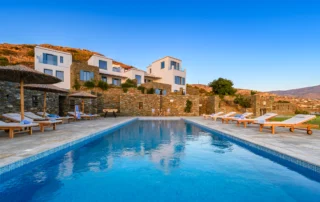 Swimming pool reflecting the evening sky below the white and stone buildings at Villa Golden Beach in Andros, Greece
