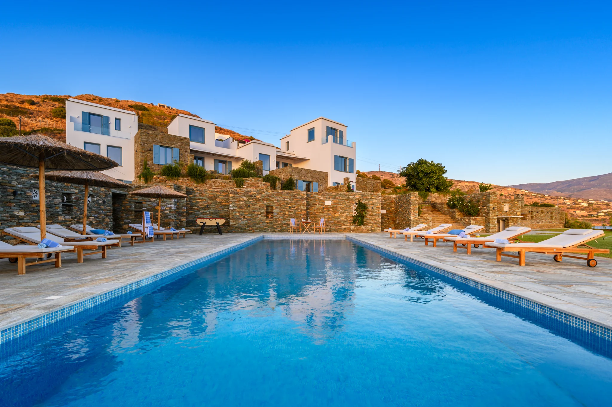 Swimming pool reflecting the evening sky below the white and stone buildings at Villa Golden Beach in Andros, Greece
