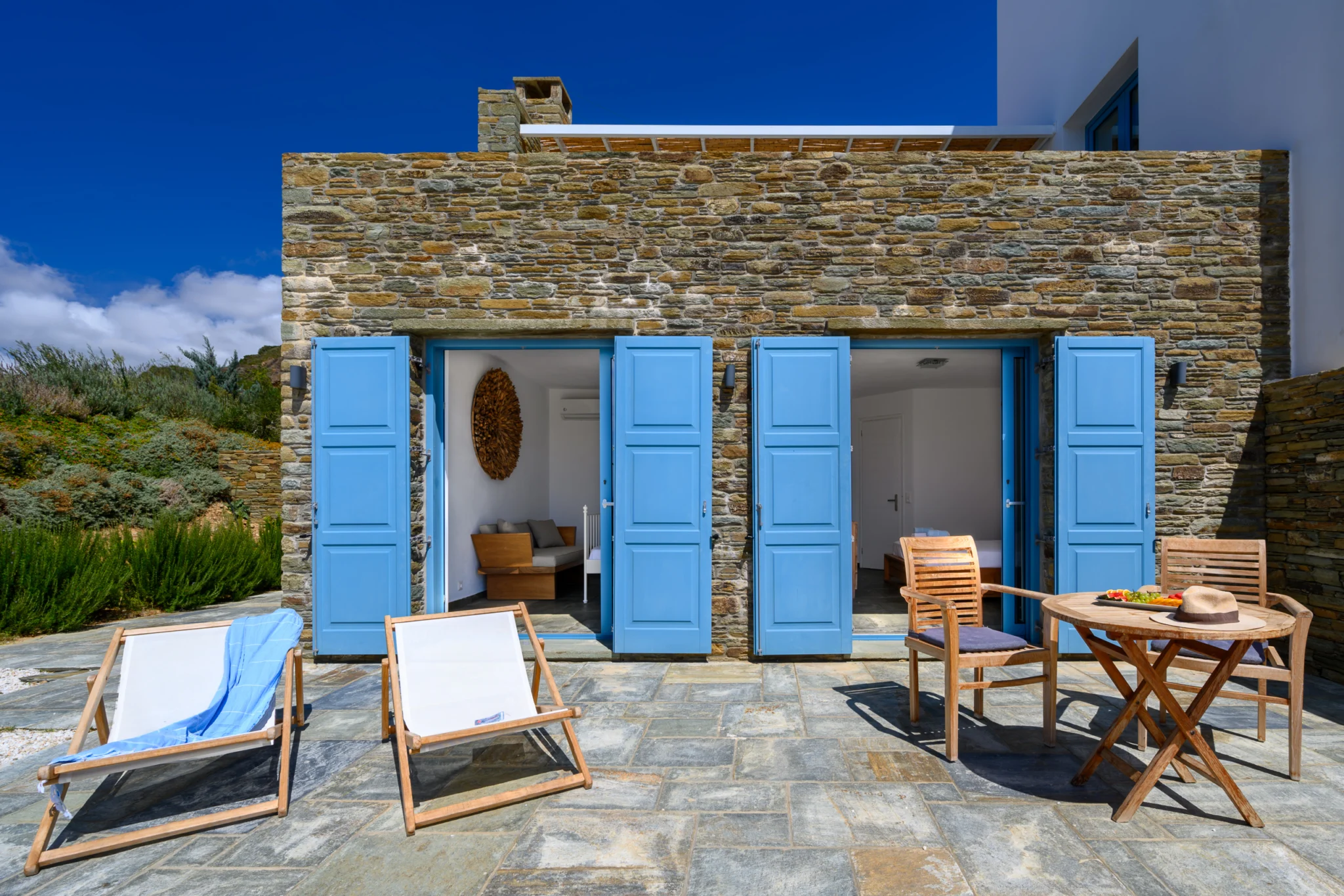 Villa Golden Beach — Stone facade and terrace, Andros Stone villa facade with open blue shutters, timber chairs and sun loungers at Villa Golden Beach in Andros