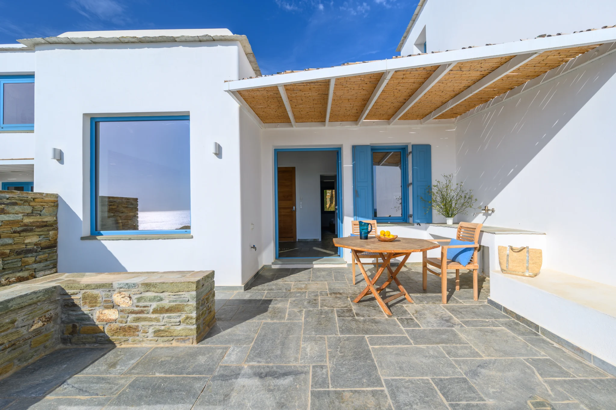 Villa Golden Beach — Shaded courtyard, Andros White courtyard with blue windows, a timber pergola and a round dining table at Villa Golden Beach in Andros
