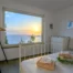 White bedroom with a large window framing sunset over the sea at Villa Hermes, Andros, Greece