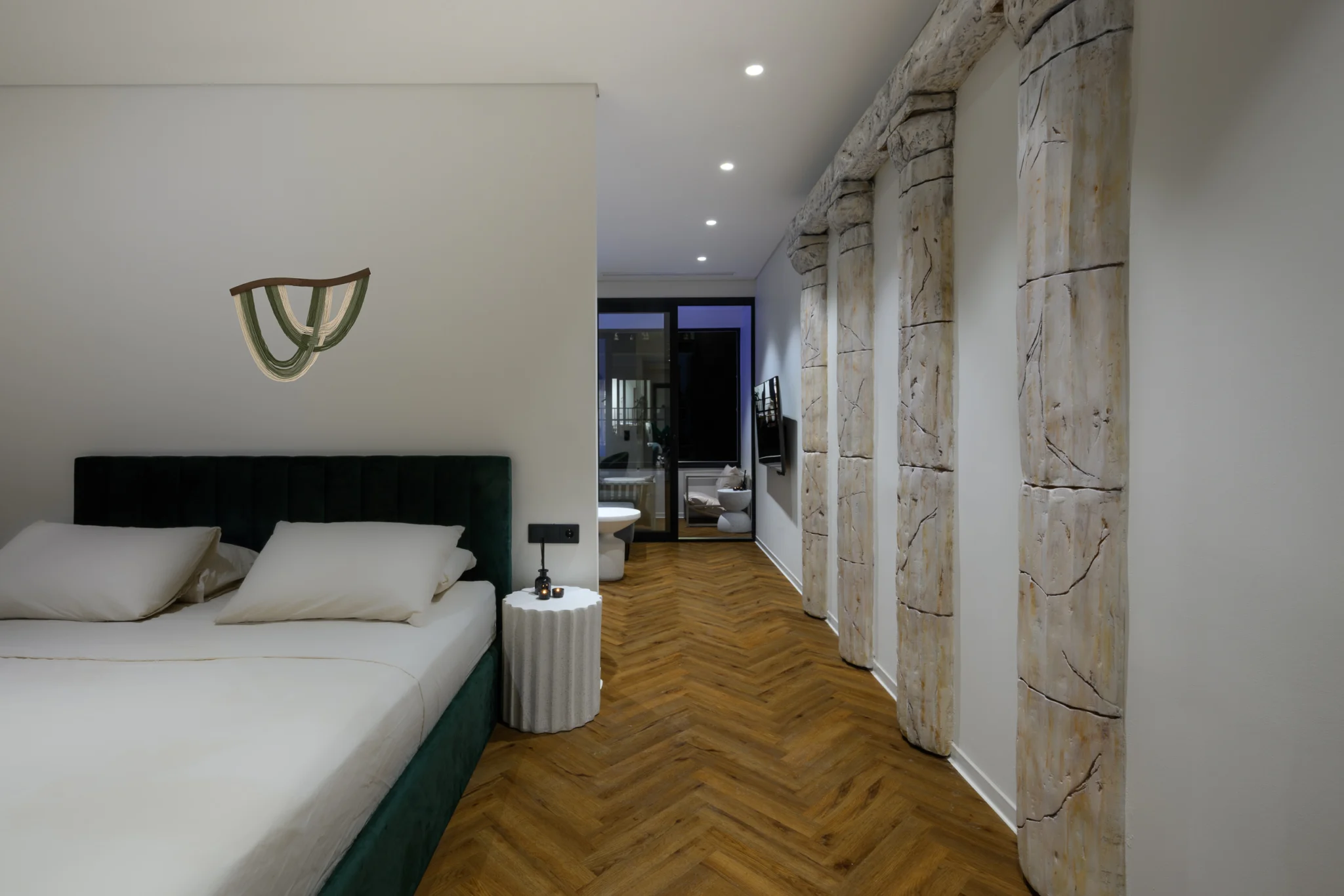 Green upholstered bed beside decorative columns, with a view towards the living area at Alpha Luxury Apartments in Athens