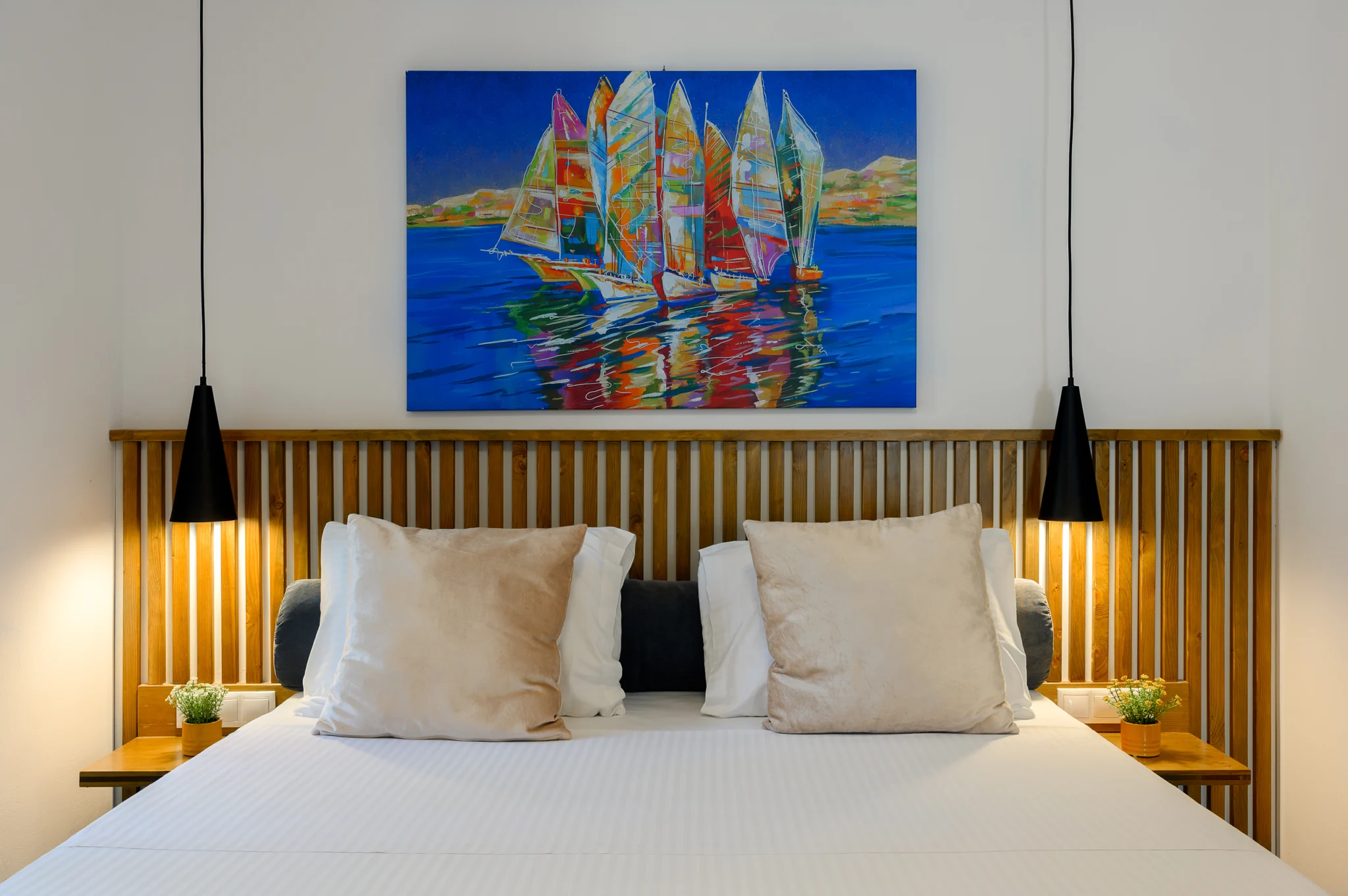 Bedroom with a timber headboard, pendant lights and sailing artwork at Blue Sky House, Pylos, Peloponnese, Greece.