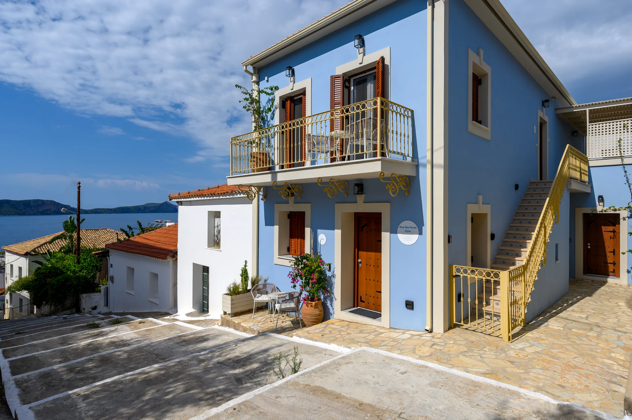 Blue house with a balcony, exterior staircase and paved forecourt at Blue Sky House, Pylos, Peloponnese, Greece.