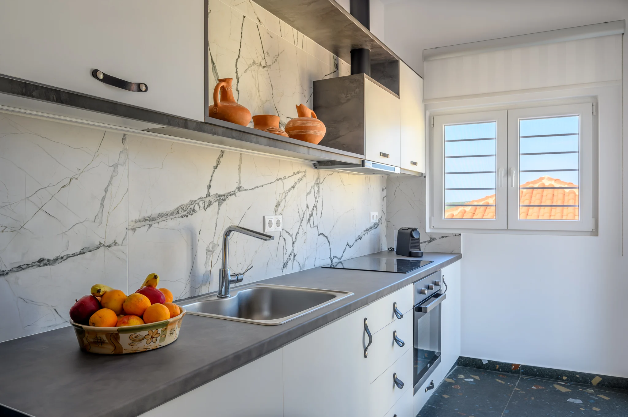 Kitchen with dark worktop, marble-effect splashback and white shutters at Blue Sky House, Pylos, Peloponnese, Greece.