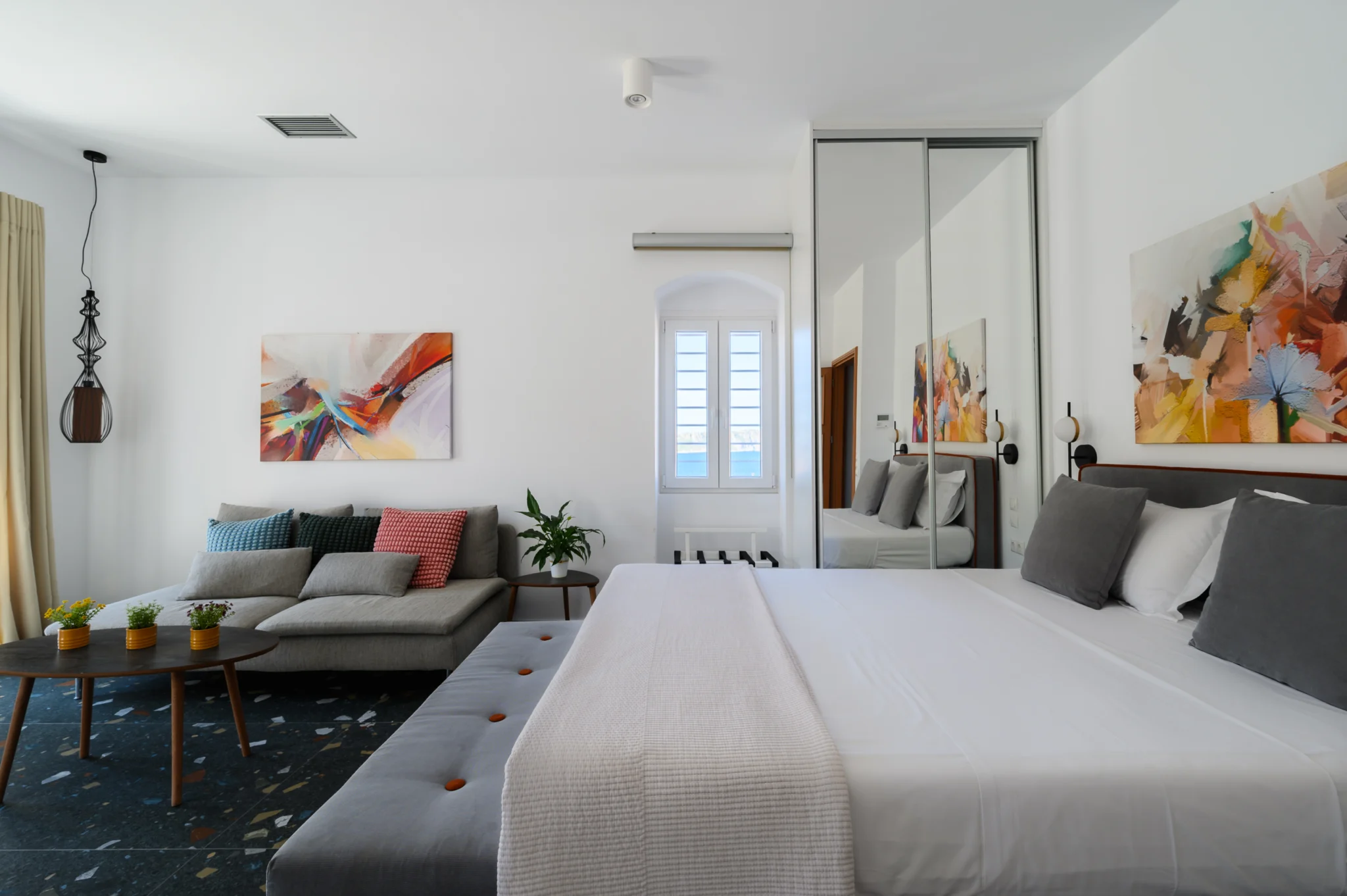 Bedroom and lounge with grey seating and colourful artwork at Blue Sky House, Pylos, Peloponnese, Greece.