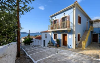 Blue house and paved forecourt framed by an olive tree at Blue Sky House, Pylos, Peloponnese, Greece.