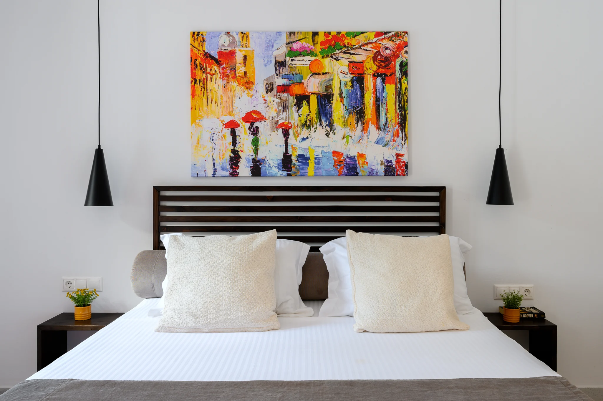Bedroom with dark timber headboard, pendant lights and colourful artwork at Blue Sky House, Pylos, Peloponnese, Greece.