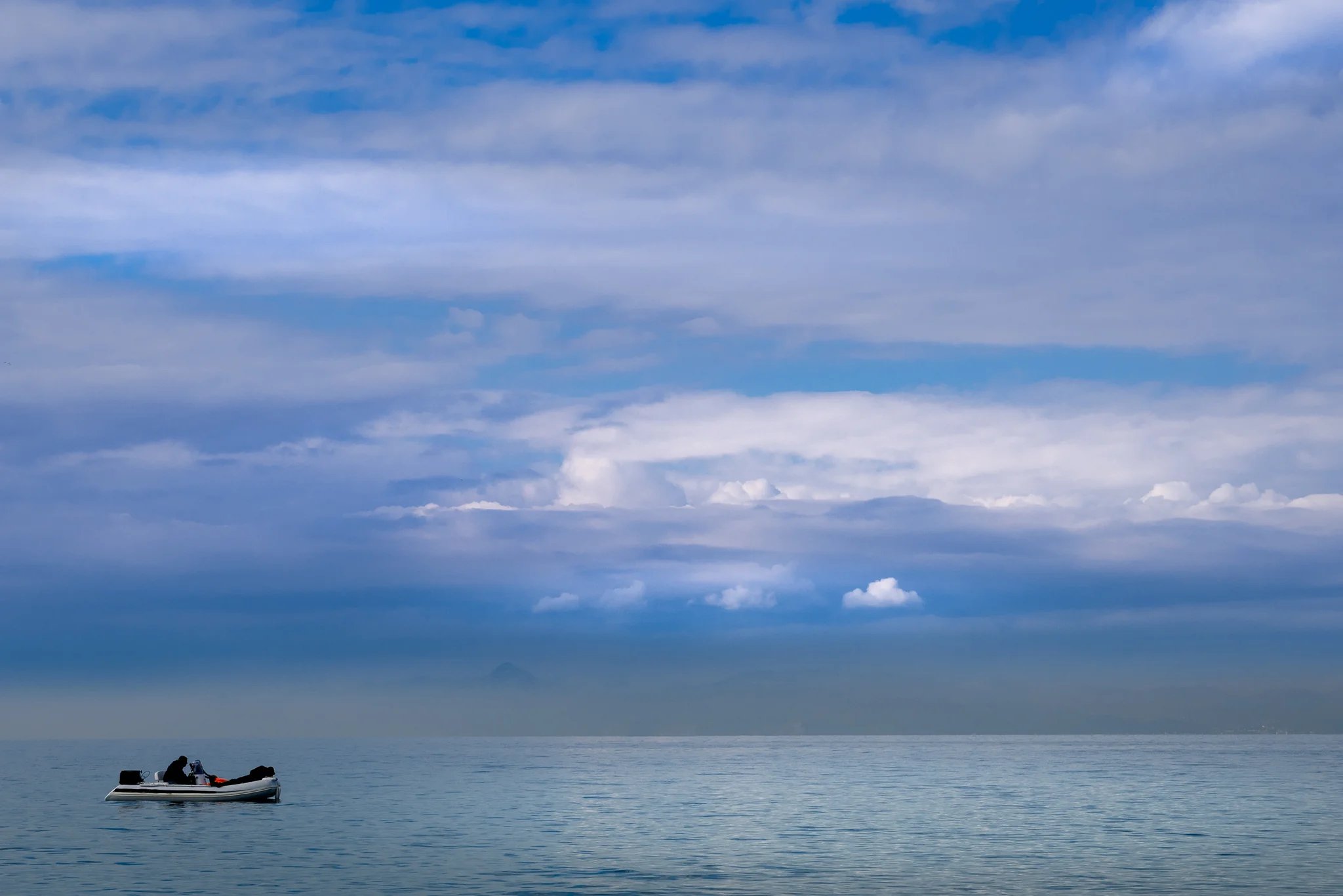 Small motorboat crossing calm sea beneath layered storm clouds