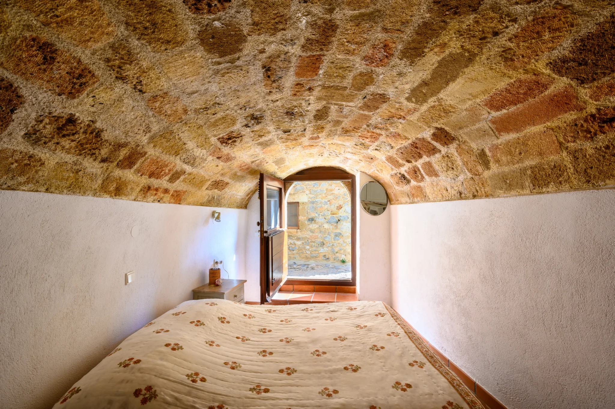 Bedroom with white plaster walls beneath a stone vaulted ceiling, facing an open arched timber door at Castle Residence in Monemvasia.