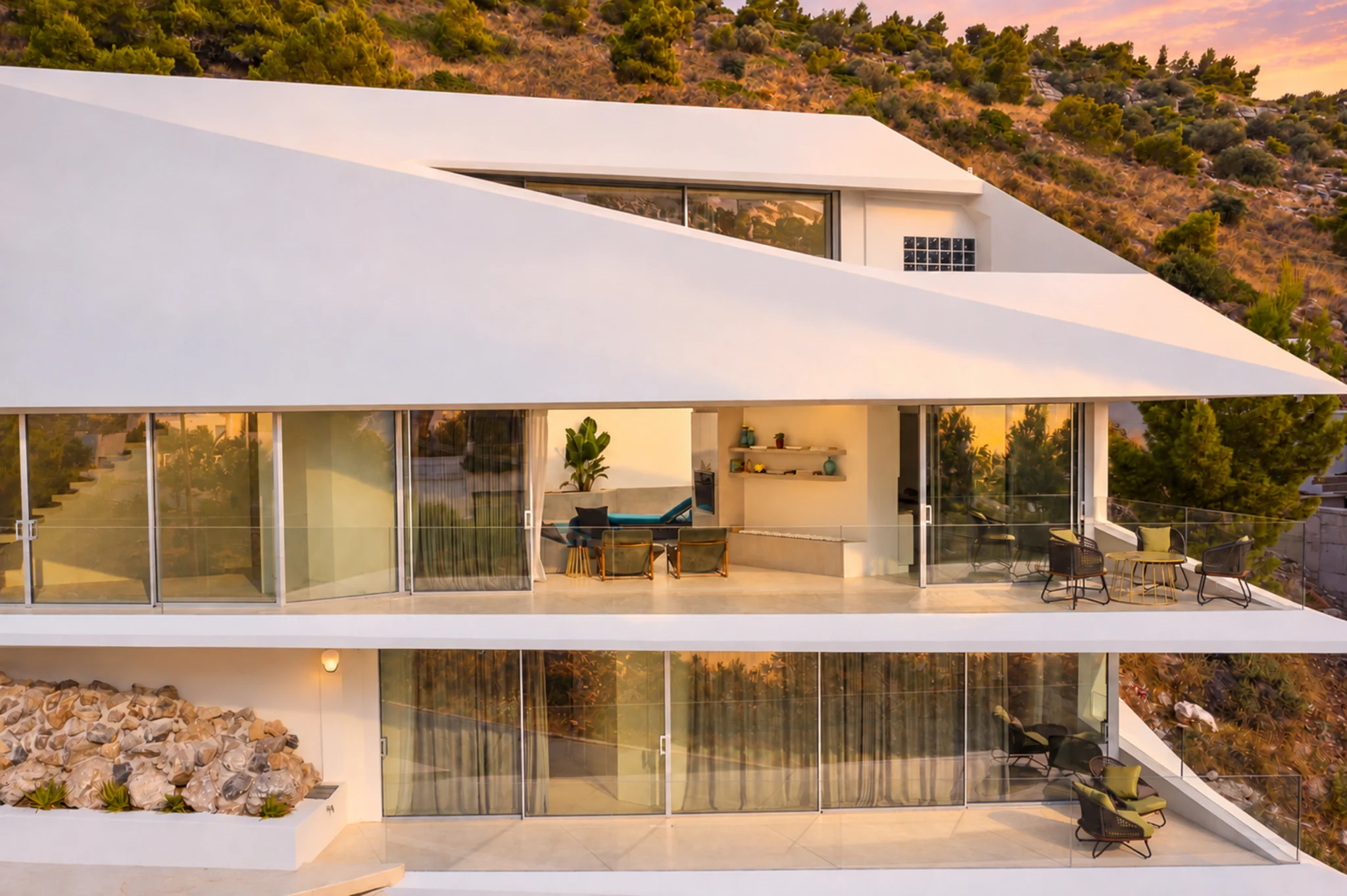 Aerial view of the angular white facade and glazed living area at sunset at Contemporary Minimalistic Villa, Athens, Attica, Greece.