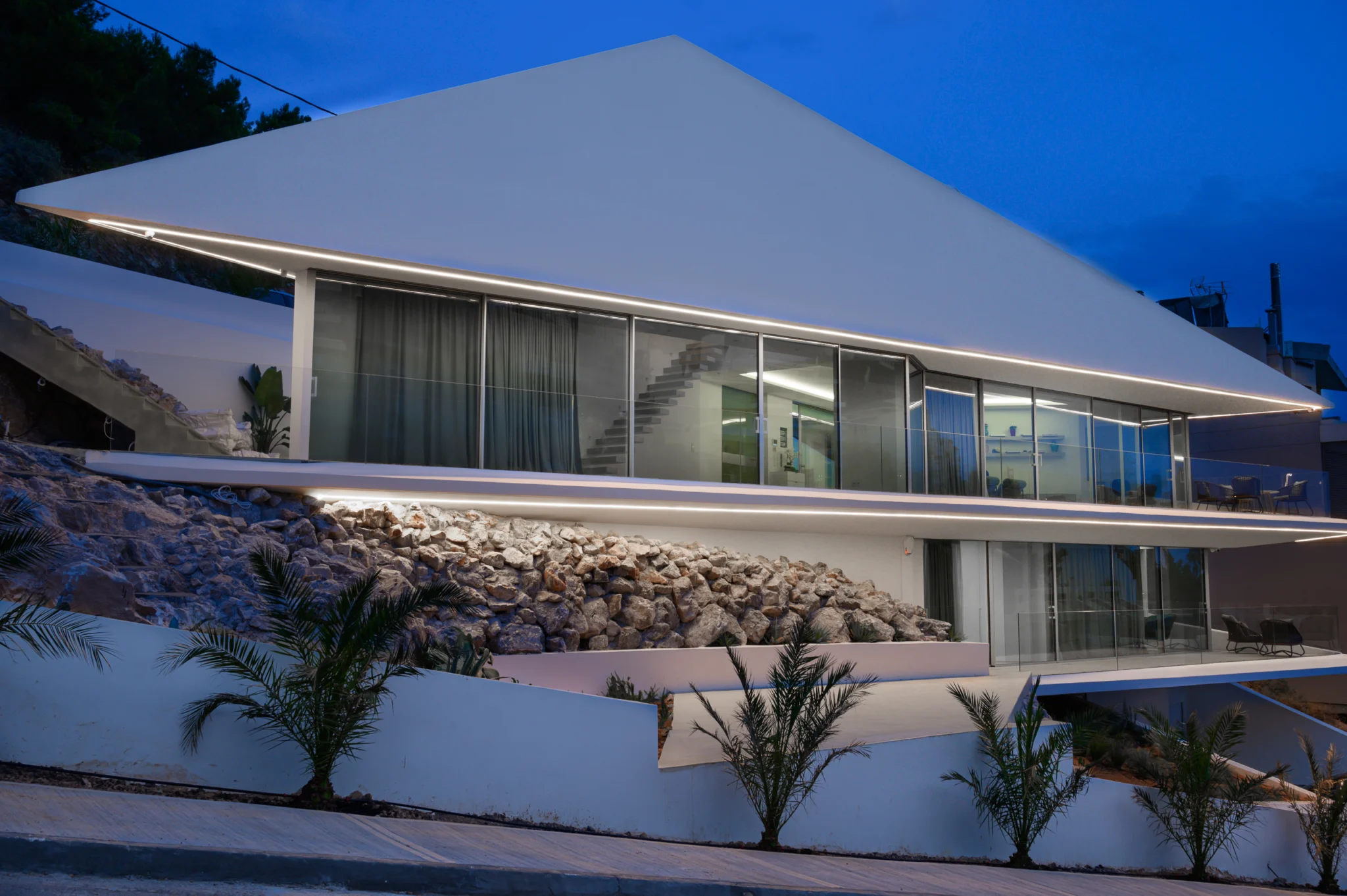 Angular white facade with illuminated roofline at twilight at Contemporary Minimalistic Villa, Athens, Attica, Greece.