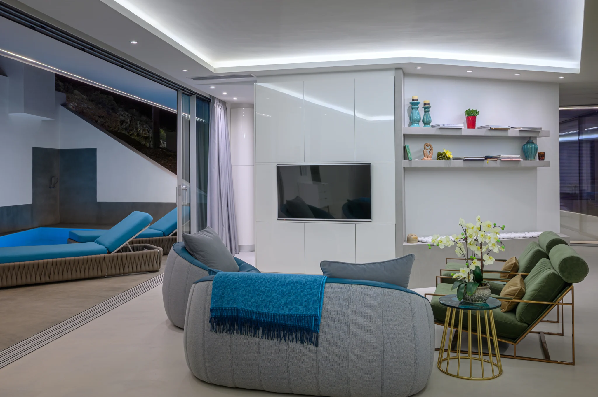 Living room with curved teal seating and ceiling lighting at night at Contemporary Minimalistic Villa, Athens, Attica, Greece.