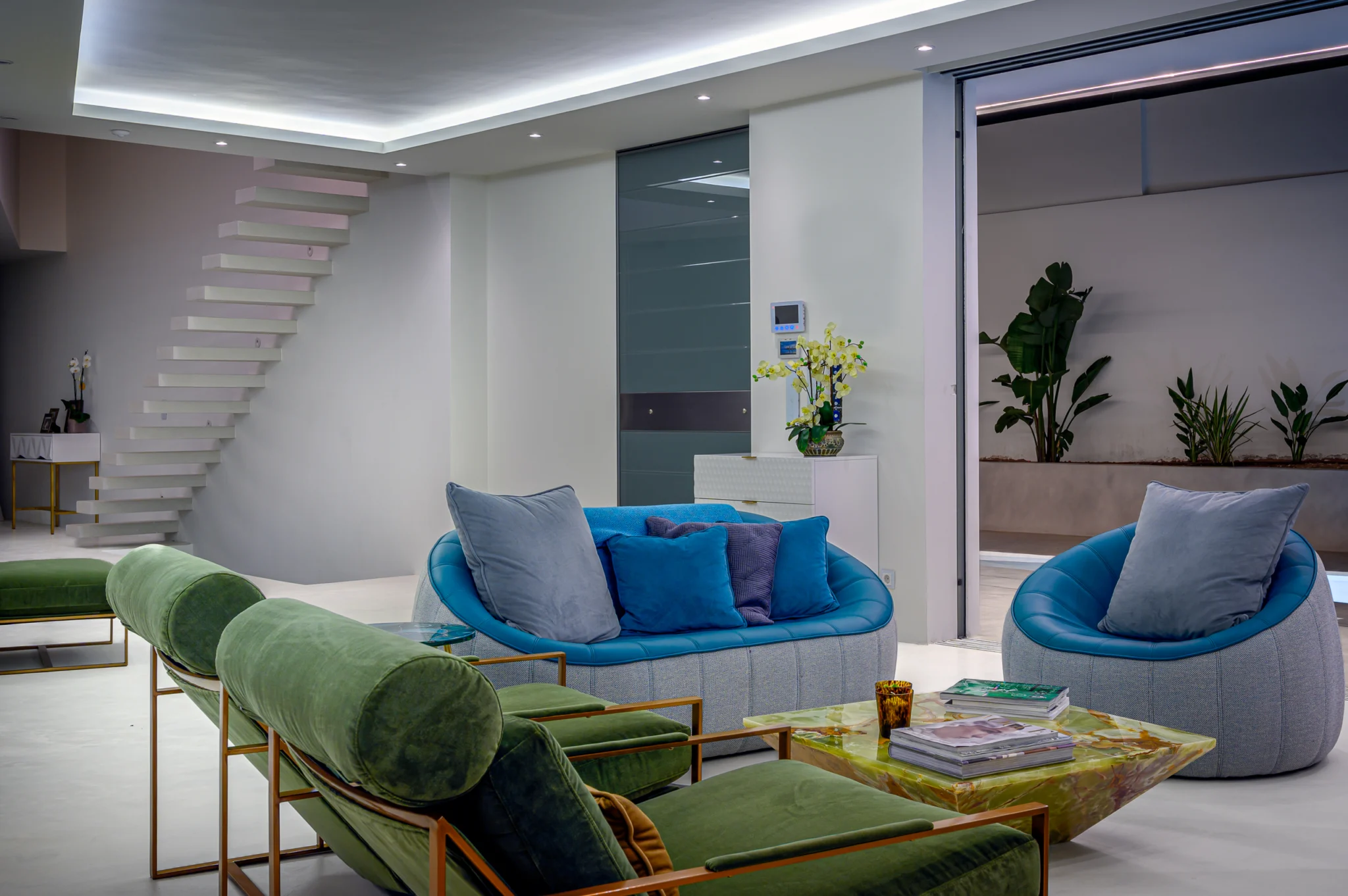 Teal and green seating with a staircase and ceiling lighting at night at Contemporary Minimalistic Villa, Athens, Attica, Greece.