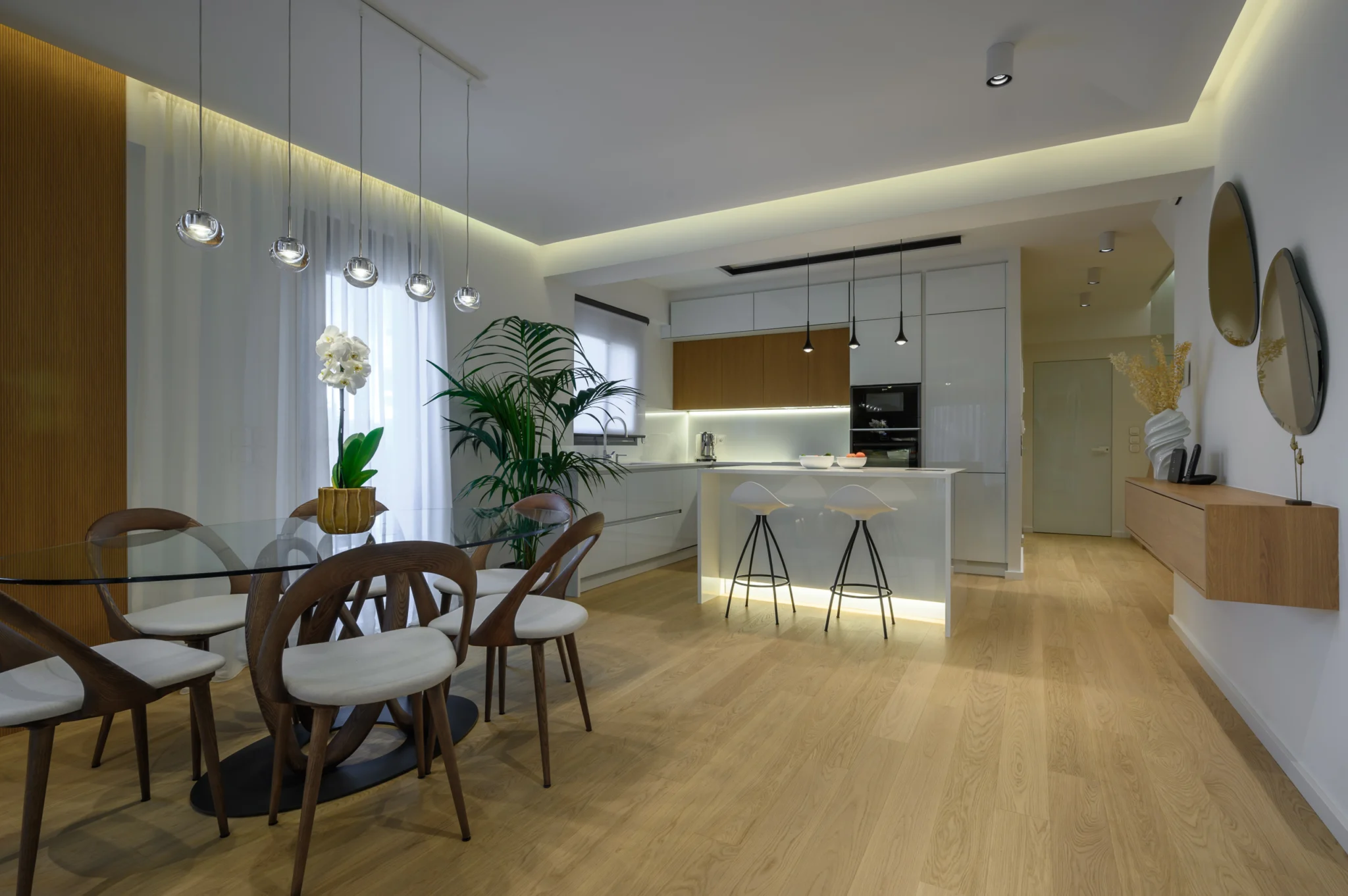 FOUNTIS apartment, Northern Athens — Open dining area with curved timber chairs, glass table and adjoining white kitchen Open dining area with curved timber chairs, glass table and adjoining white kitchen in a luxury apartment in northern Athens.