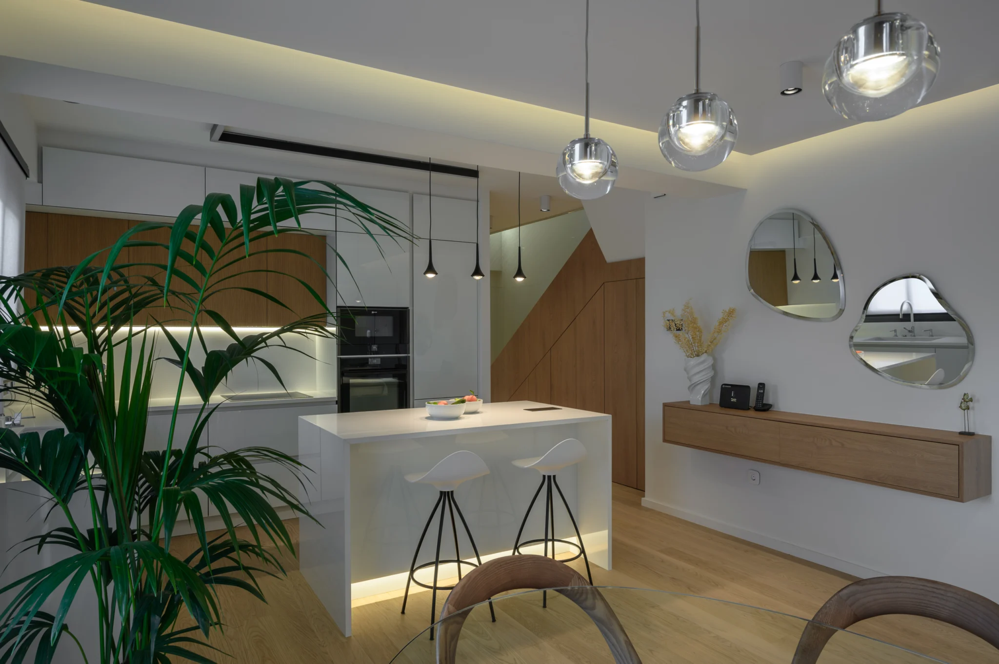 FOUNTIS apartment, Northern Athens — Kitchen island and pendant lighting viewed past a plant towards organic mirrors Kitchen island and pendant lighting viewed past a plant towards organic mirrors in a luxury apartment in northern Athens.