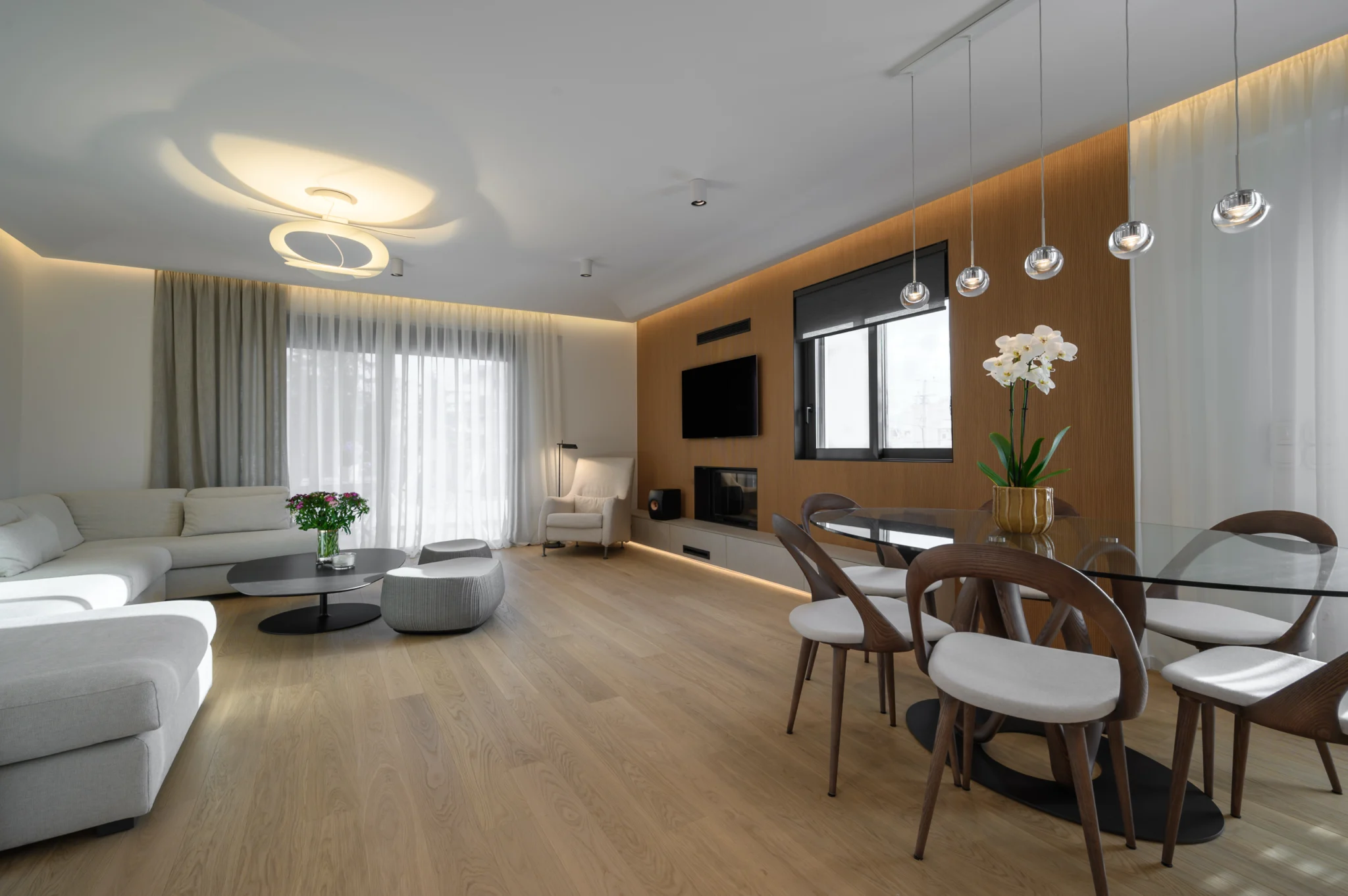 FOUNTIS apartment, Northern Athens — Living and dining area with pale seating and a timber television and fireplace wall Living and dining area with pale seating and a timber television and fireplace wall in a luxury apartment in northern Athens.
