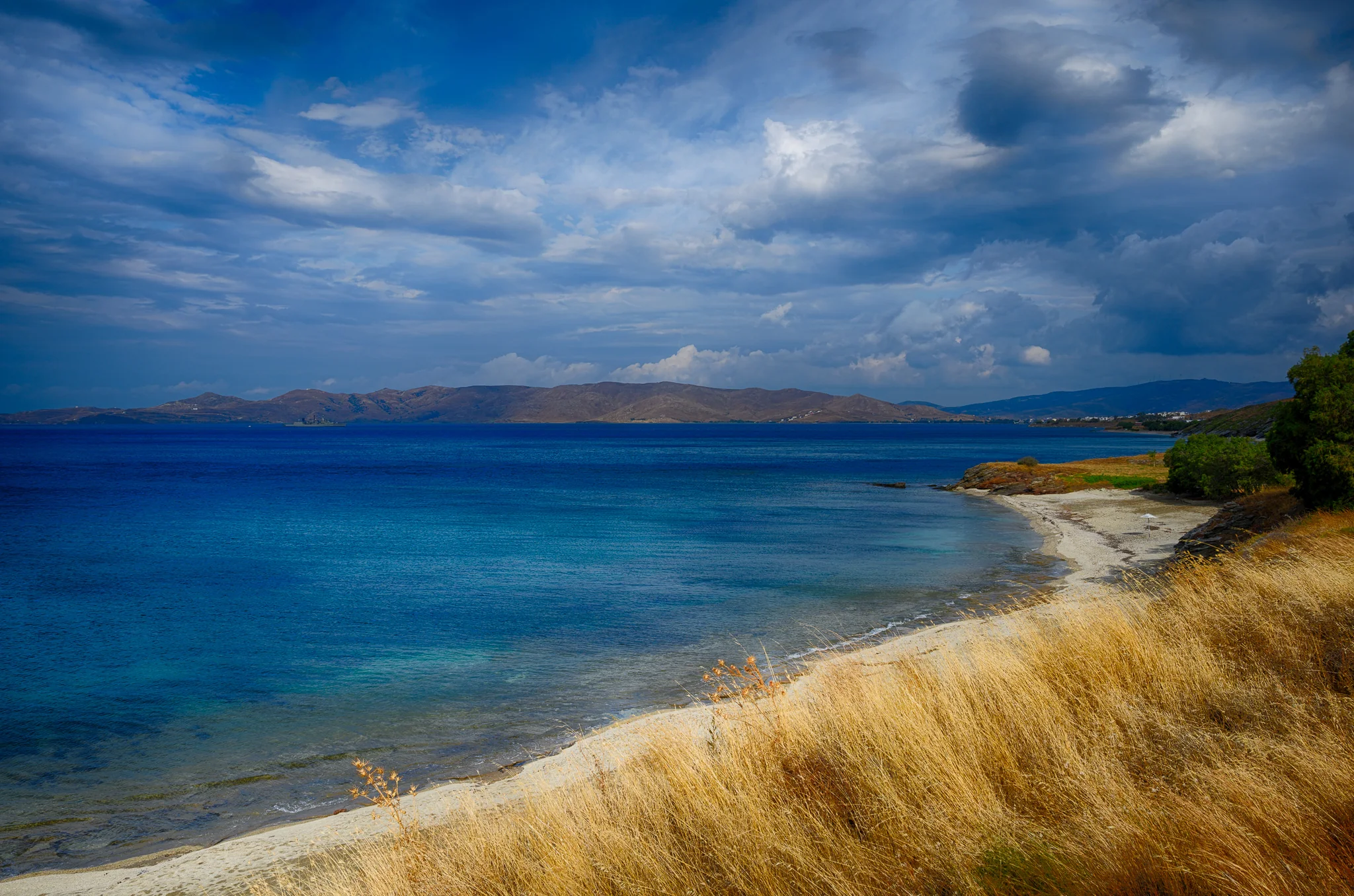 Quiet Greek island cove with golden grass blue water and gathering storm clouds