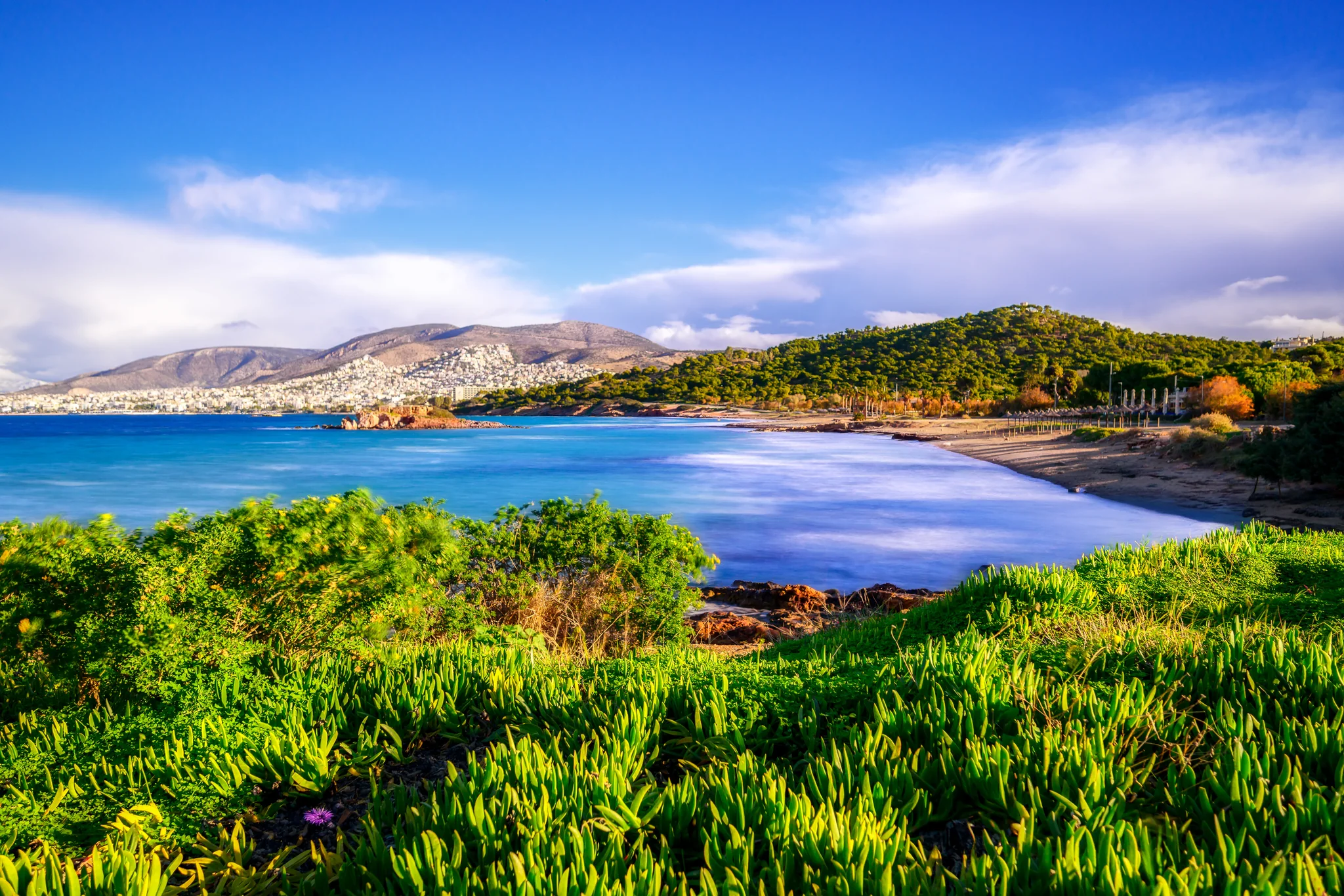 Green coastal bay with calm blue water beach and wooded headland