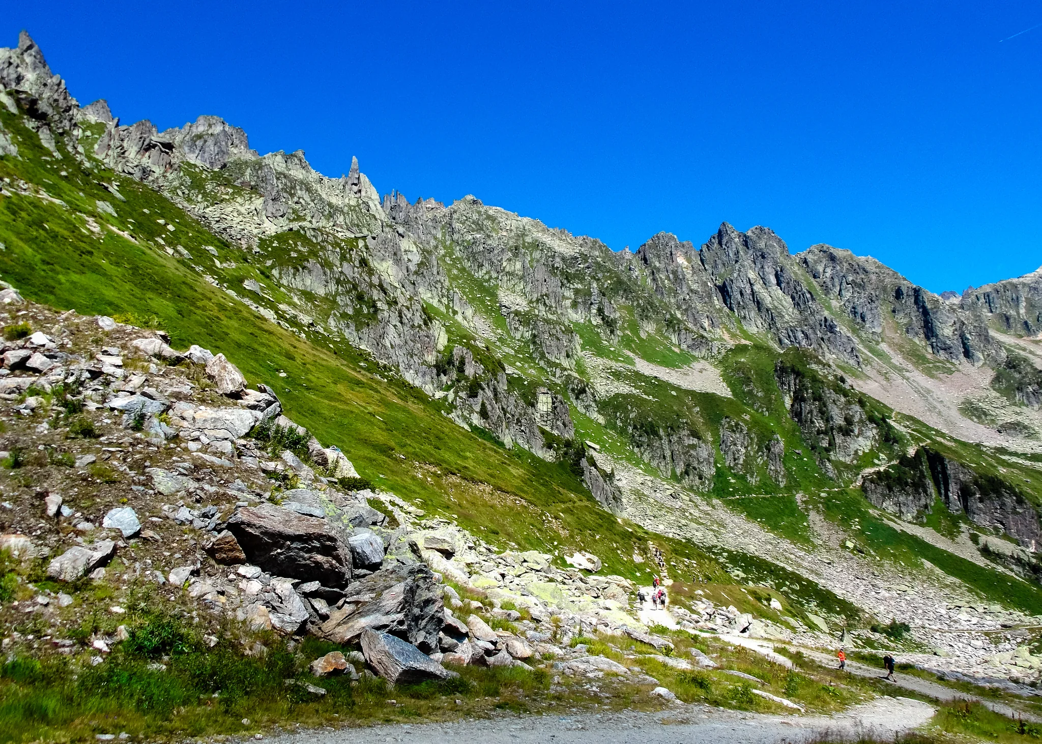 Hikers crossing a green rocky ridge in the high Alps