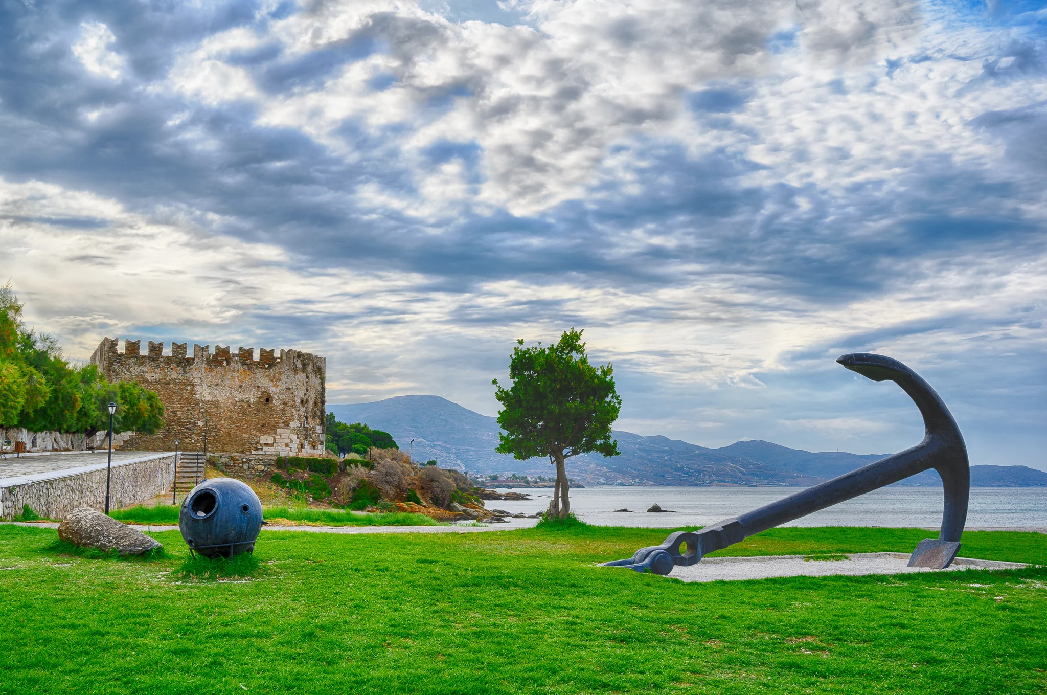 Historic crenellated stone tower and large maritime anchor beside a coastal bay