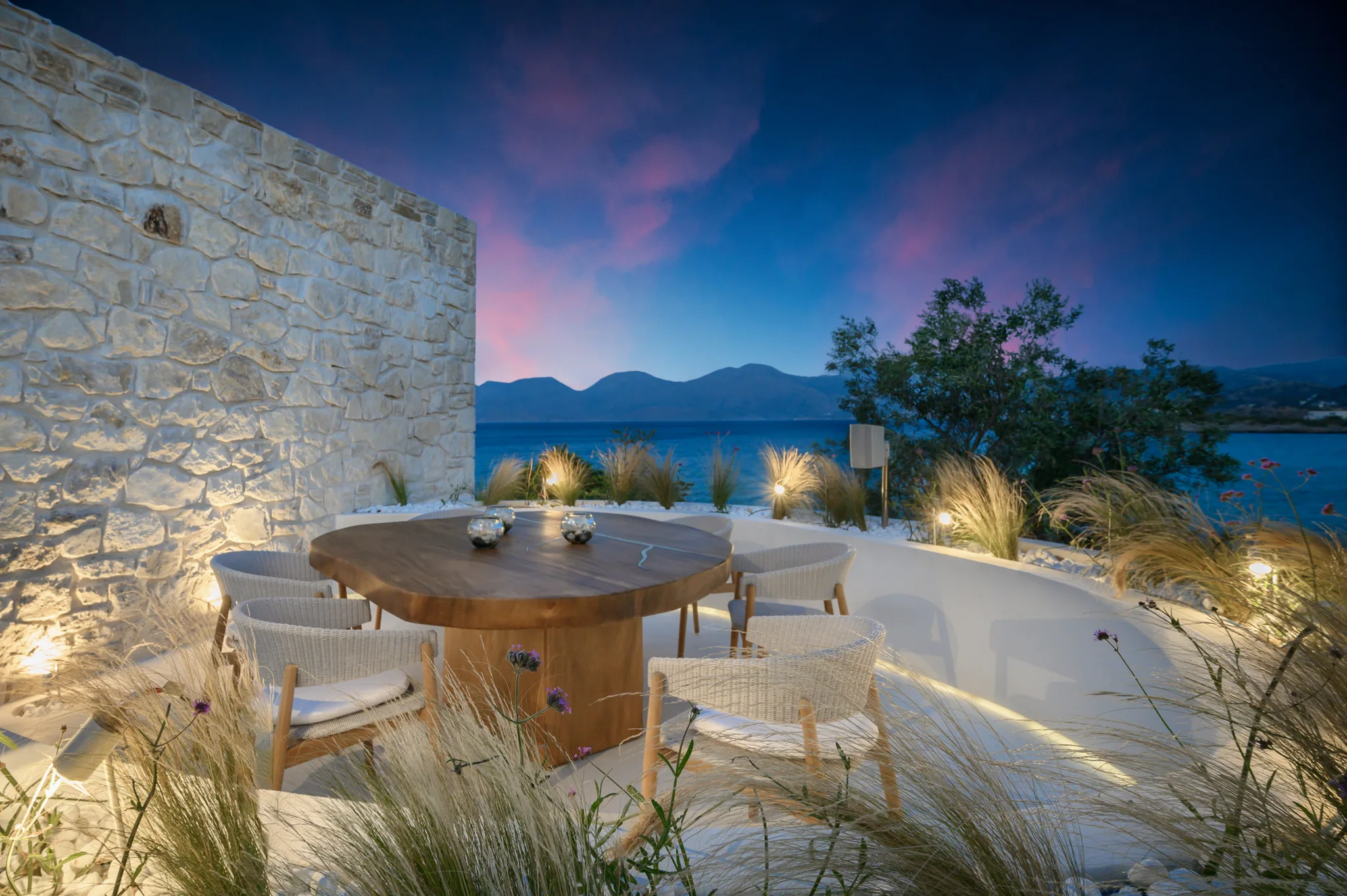 Stone hotel terrace with a round dining table beside water at dusk