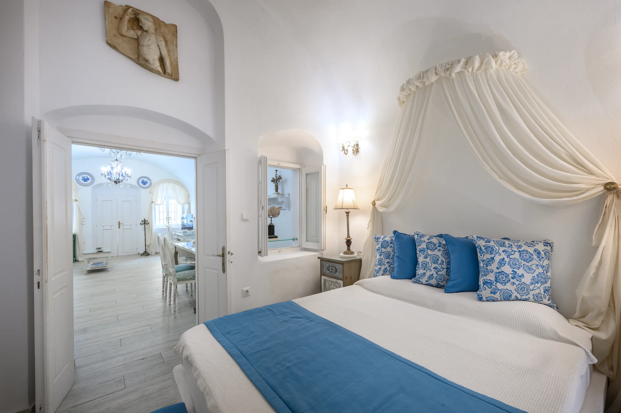 Intermezzo, Santorini — Angled bedroom view with a draped canopy and a doorway to the adjoining living space Angled bedroom view with a draped canopy and a doorway to the adjoining living space at Intermezzo in Santorini.