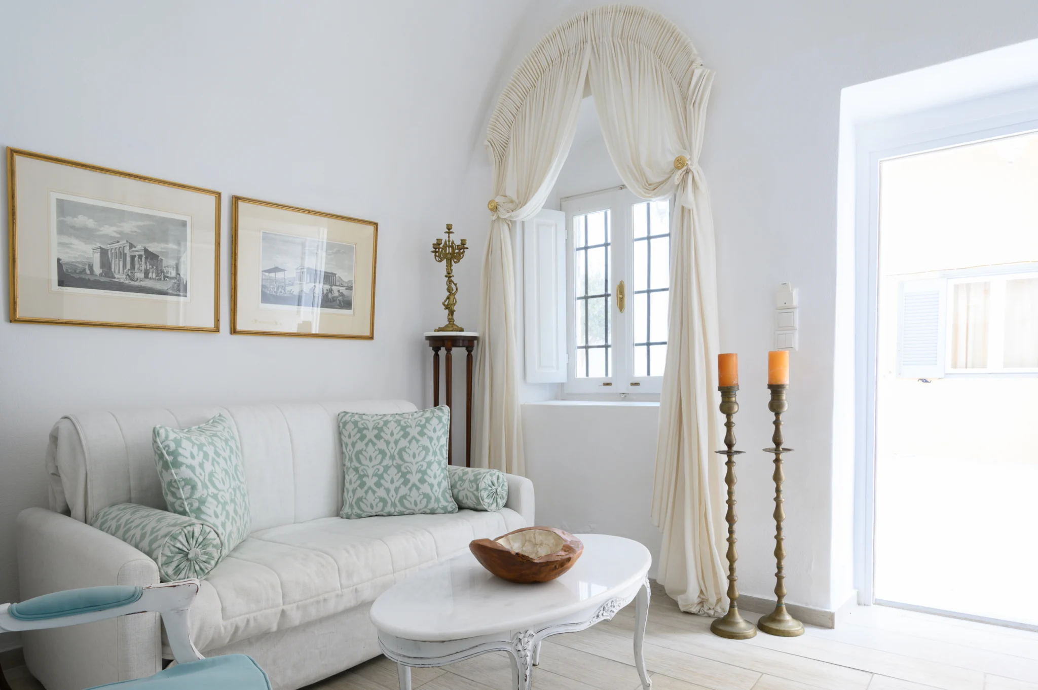Intermezzo, Santorini — Daylit sitting area with a white sofa, green patterned cushions and a curved coffee table Daylit sitting area with a white sofa, green patterned cushions and a curved coffee table at Intermezzo in Santorini.