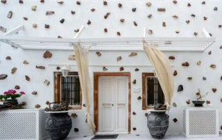 Front entrance with white pergola, flowing curtains and two large dark decorative pots at Intermezzo in Santorini.