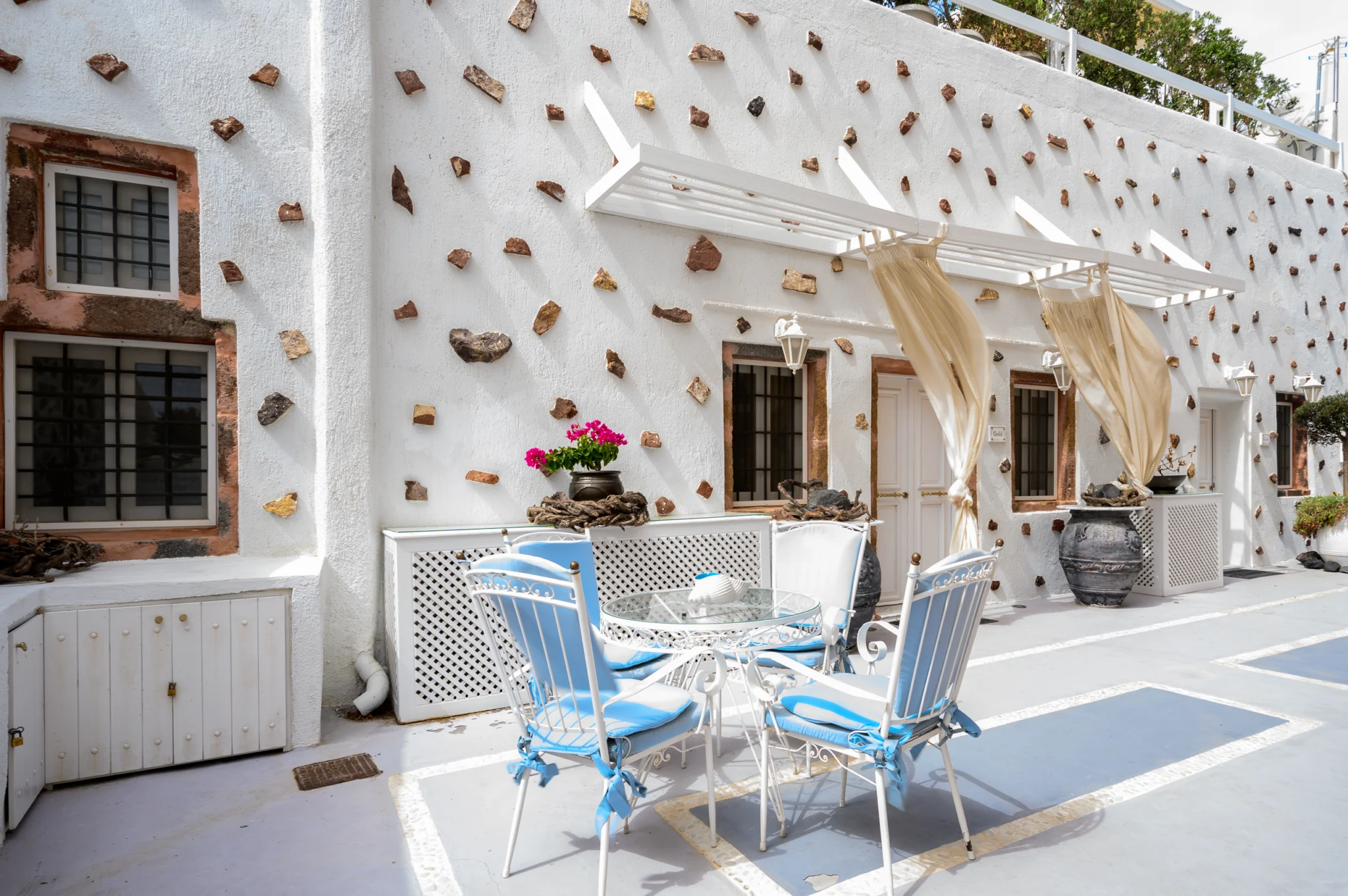 Intermezzo, Santorini — Courtyard dining table with pale blue chairs beside the textured white facade Courtyard dining table with pale blue chairs beside the textured white facade at Intermezzo in Santorini.