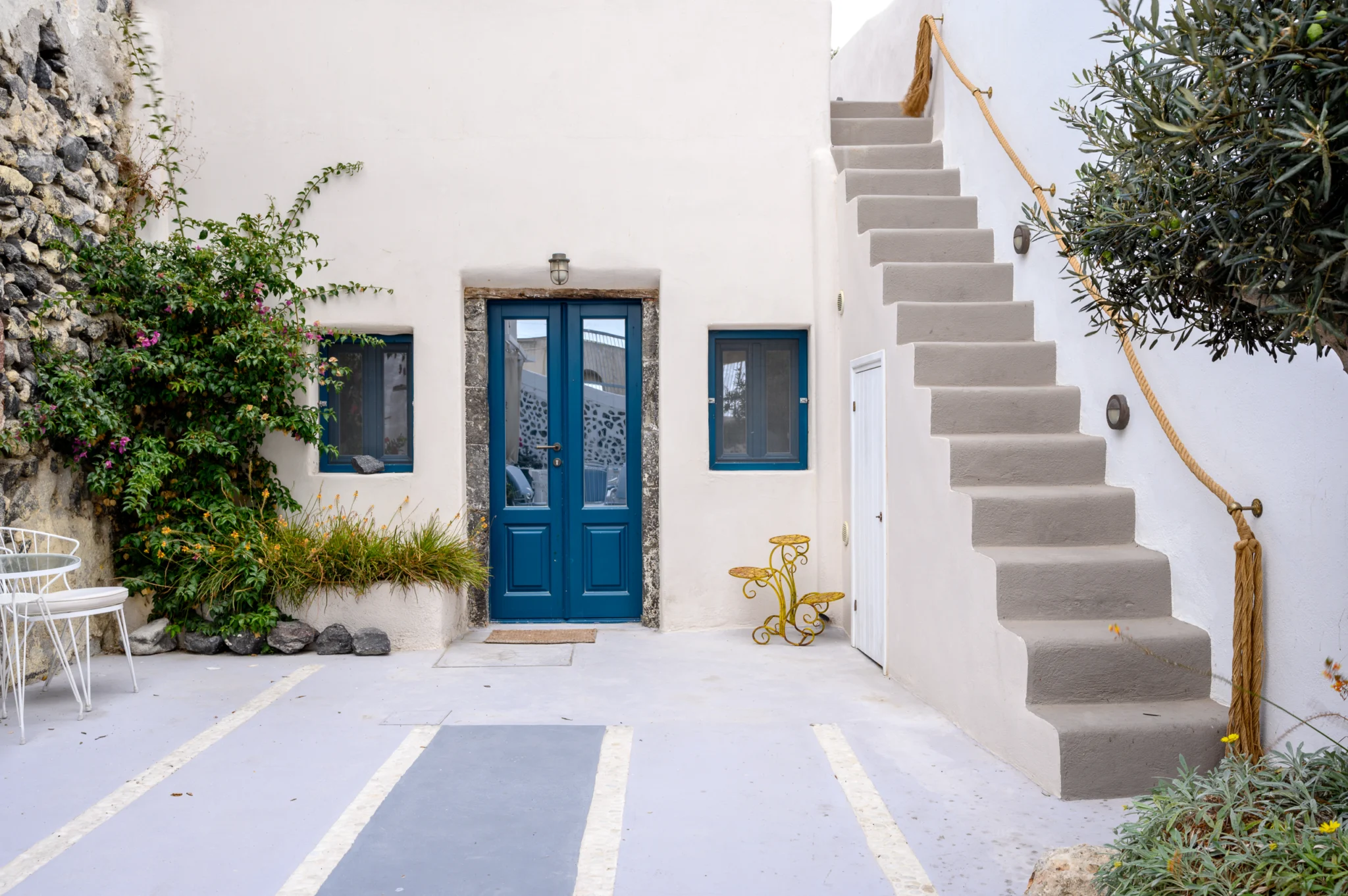 Intermezzo, Santorini — Courtyard with blue doors, planting and an exterior staircase with a rope handrail Courtyard with blue doors, planting and an exterior staircase with a rope handrail at Intermezzo in Santorini.