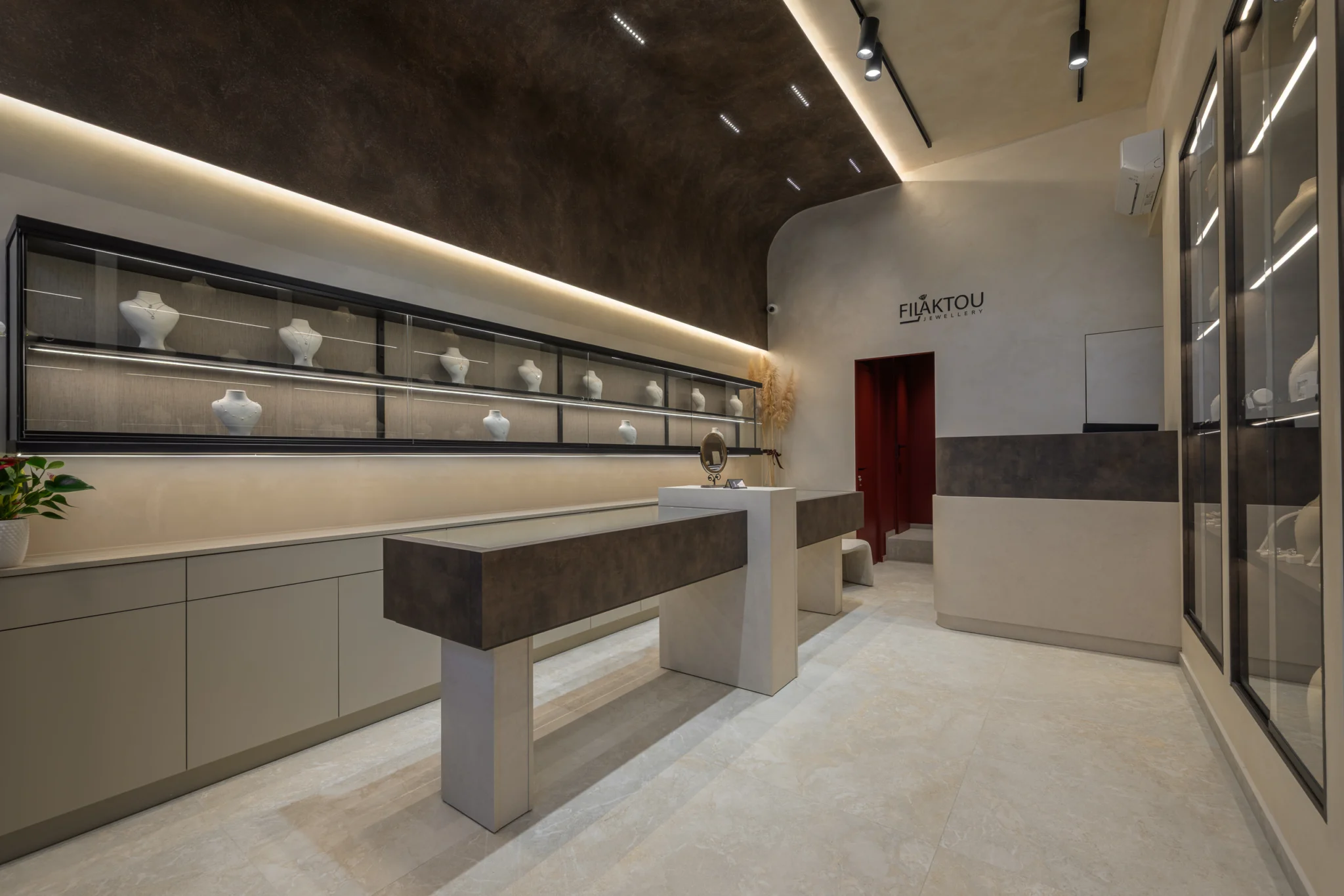 Jewelry shop interior in Korydallos, Athens, with a long illuminated wall display, freestanding counters and a curved dark ceiling.