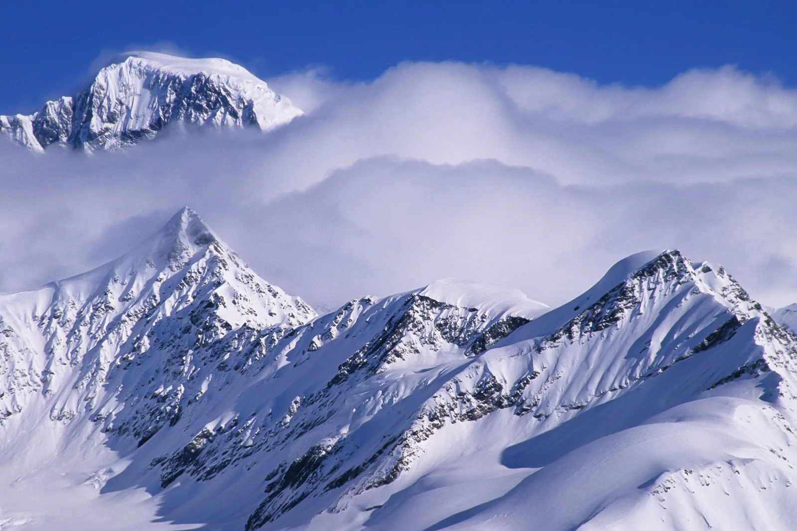 Layered snow-covered mountain peaks emerging through moving cloud