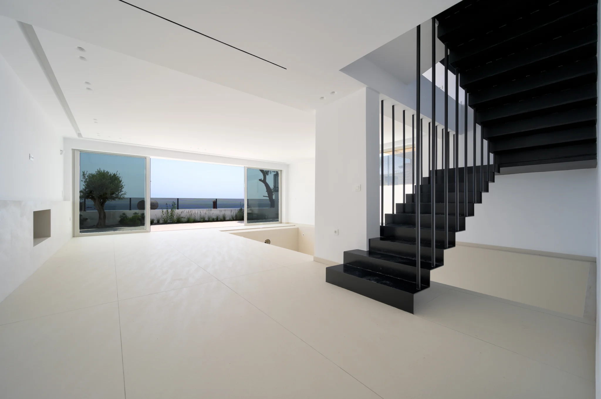 White interior with a black staircase and a wide sea-facing window at Luxury Residence Blackstone.