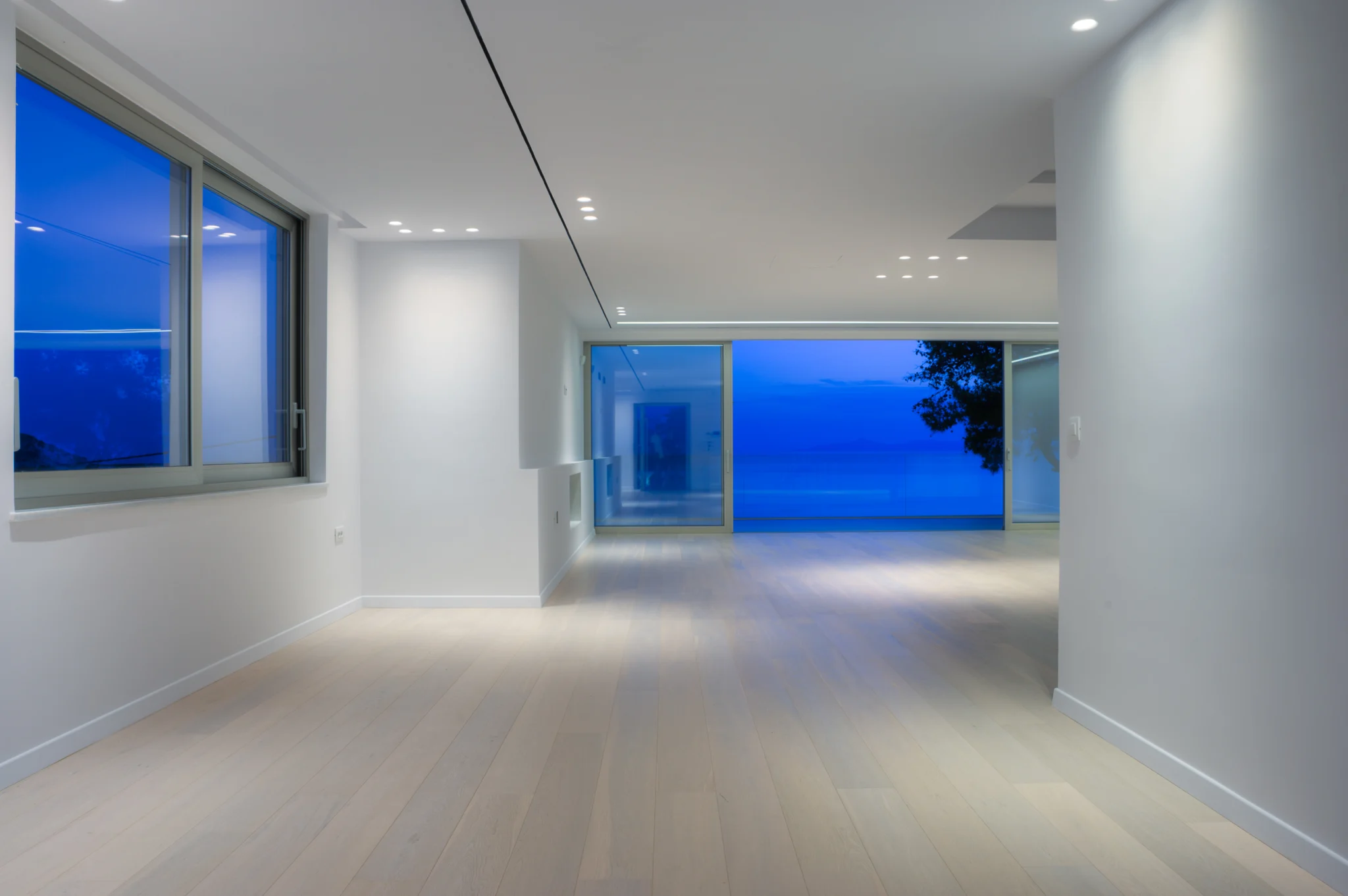 Long white interior with recessed lighting and sea-facing glazing at twilight at Luxury Residence Blackstone.