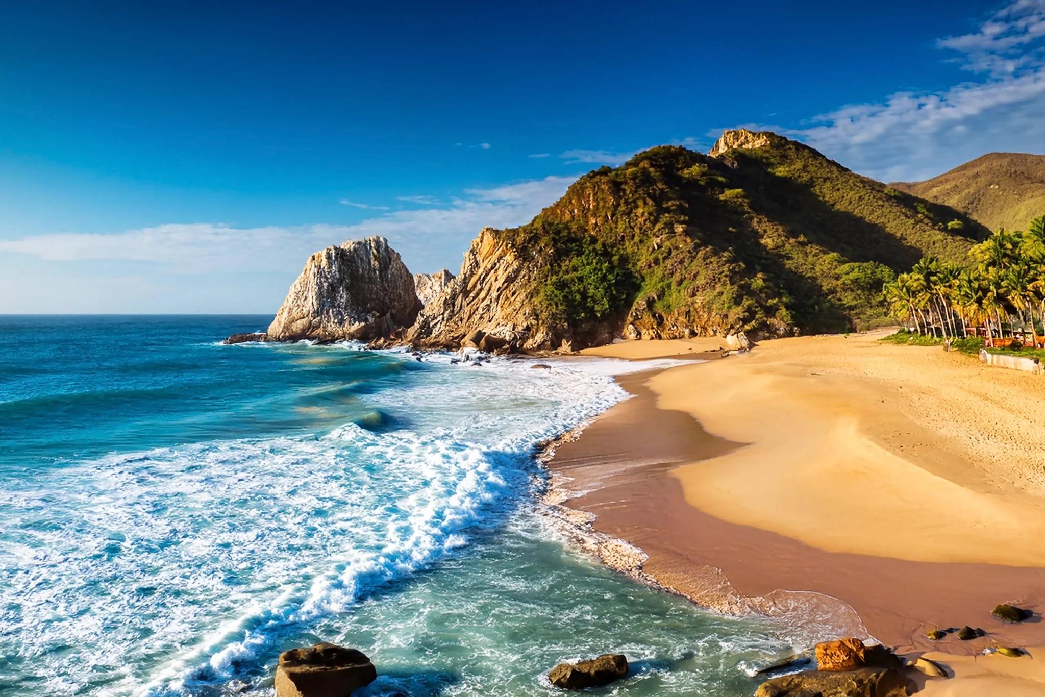 Golden beach and Pacific surf beside a rocky headland in Mazatlan Mexico