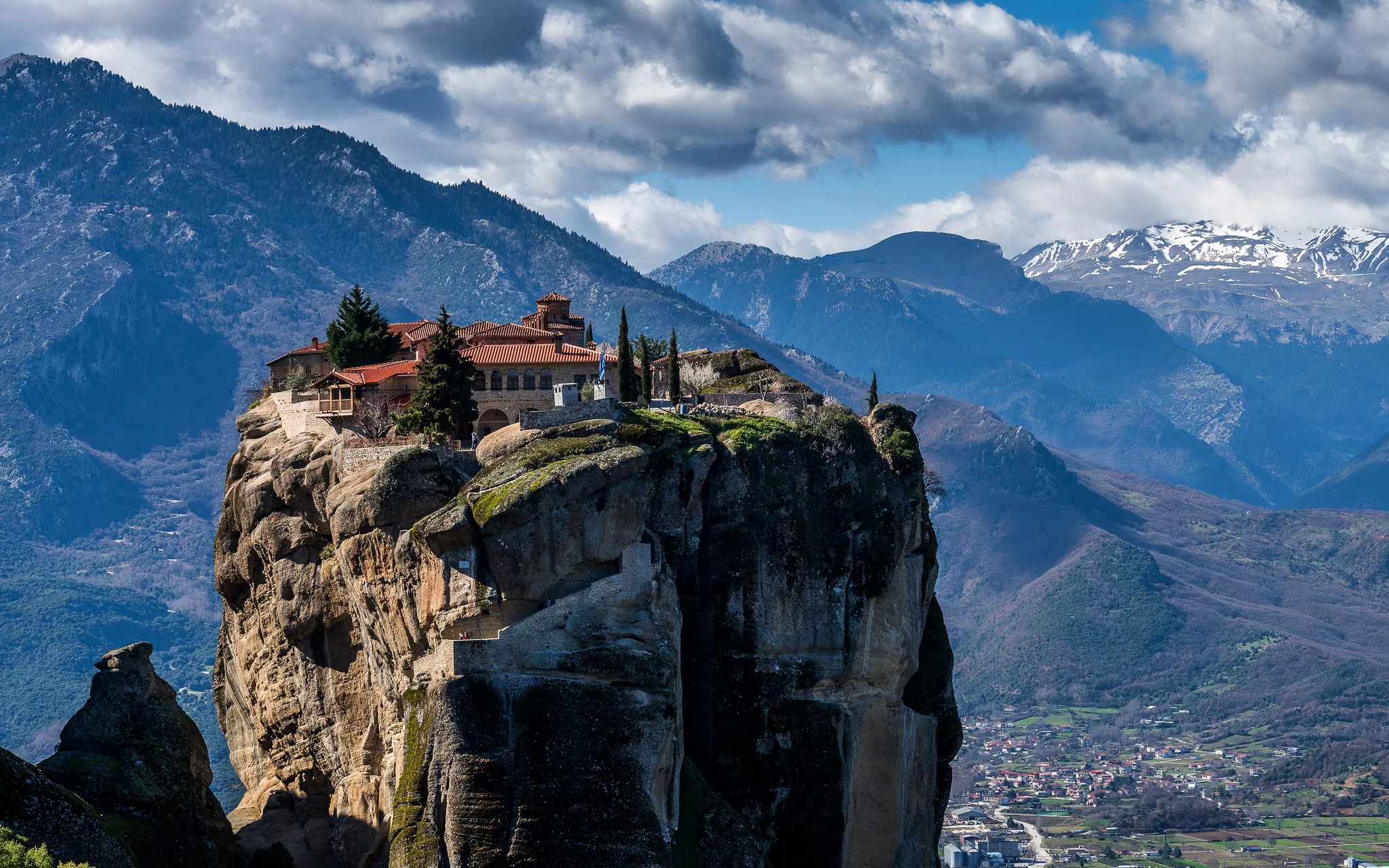 Meteora monastery on a rock pillar with snow-streaked mountains in Greece