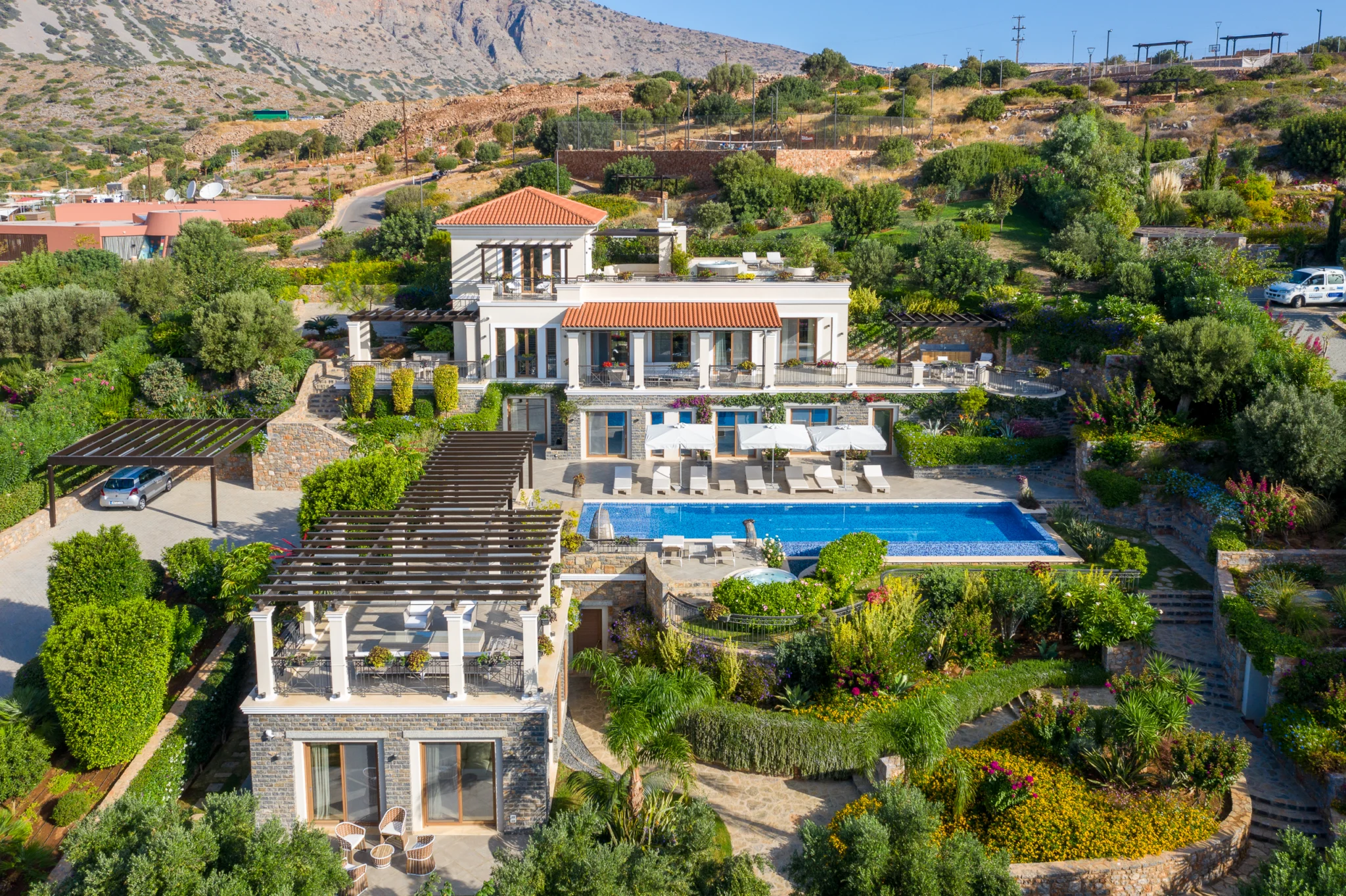 Elevated daytime view of a white villa, swimming pool and gardens at Mirum Villas, Crete, Greece