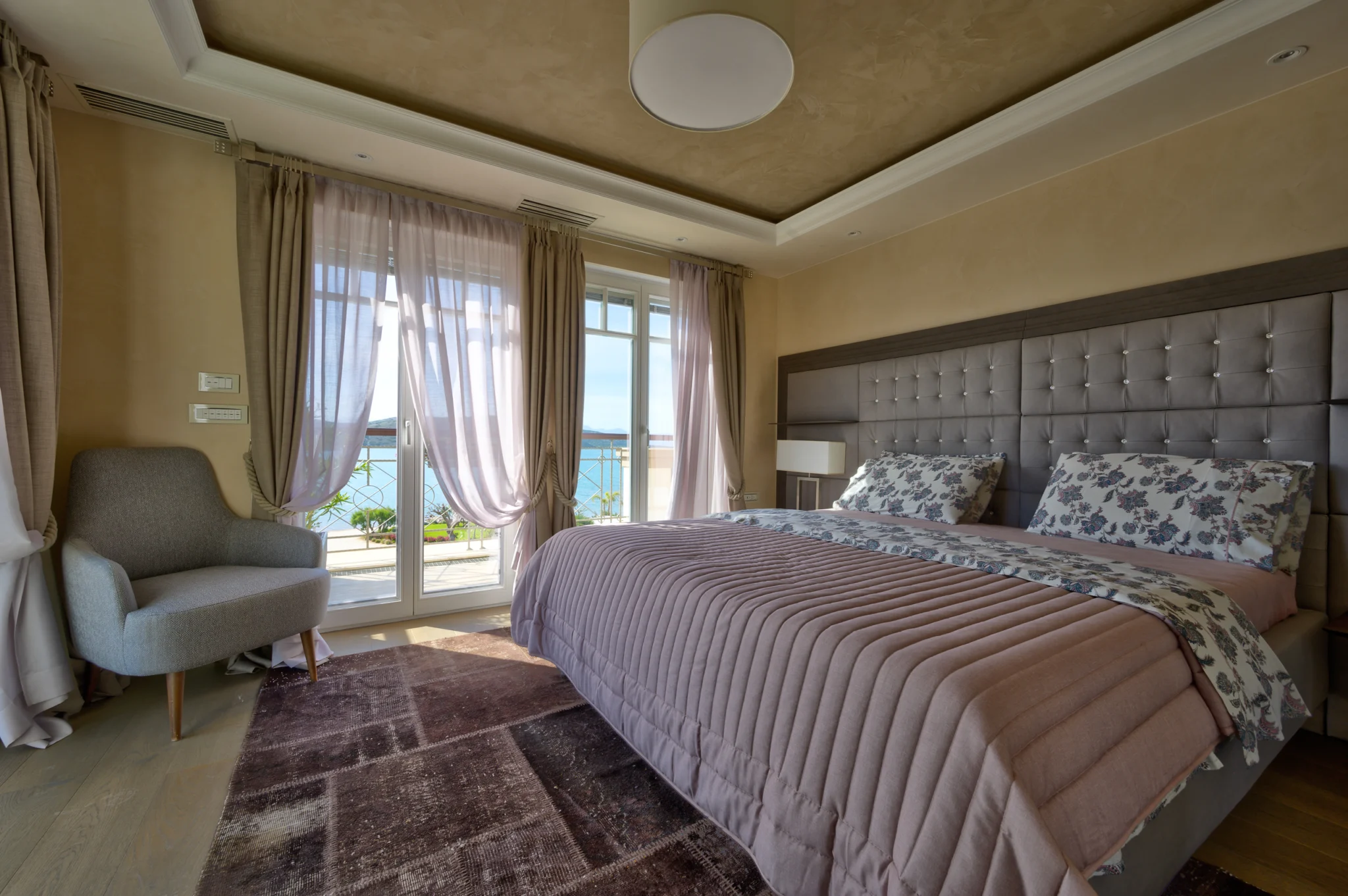 Bedroom with a pink quilt, upholstered grey headboard and armchair at Mirum Villas, Crete, Greece
