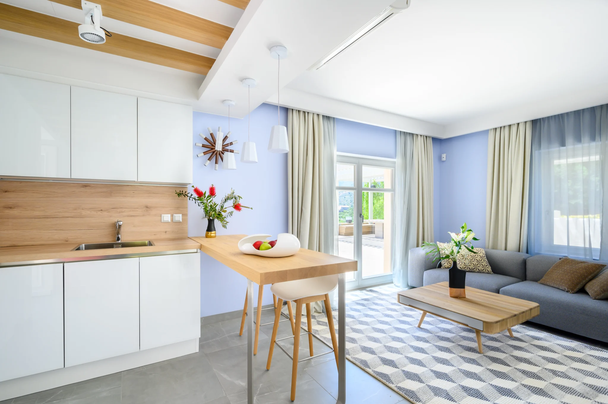 White kitchen with timber cabinets adjoining a living room at Mirum Villas, Crete, Greece
