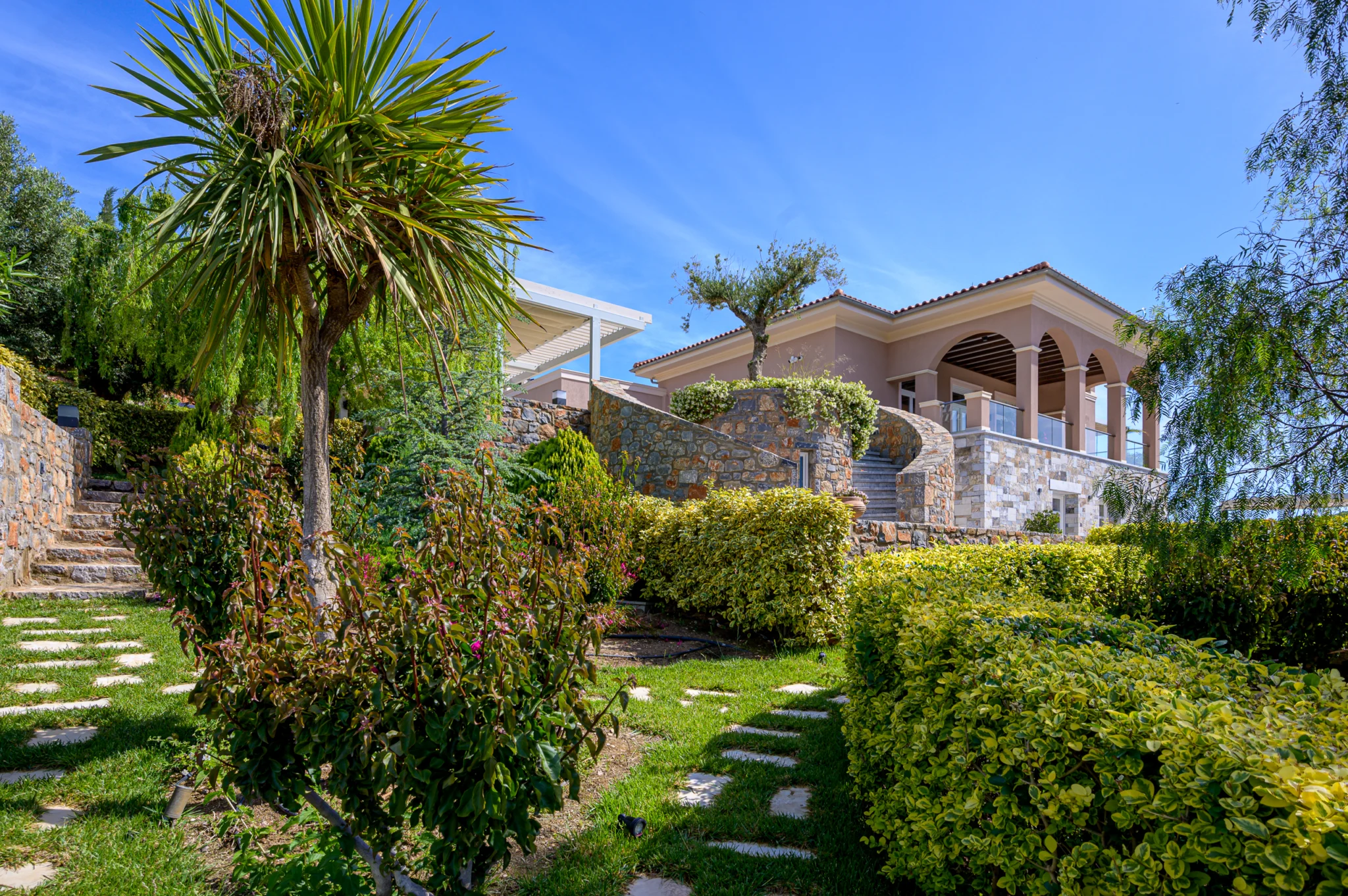 Stone villa arches above a garden with palms and pathways at Mirum Villas, Crete, Greece