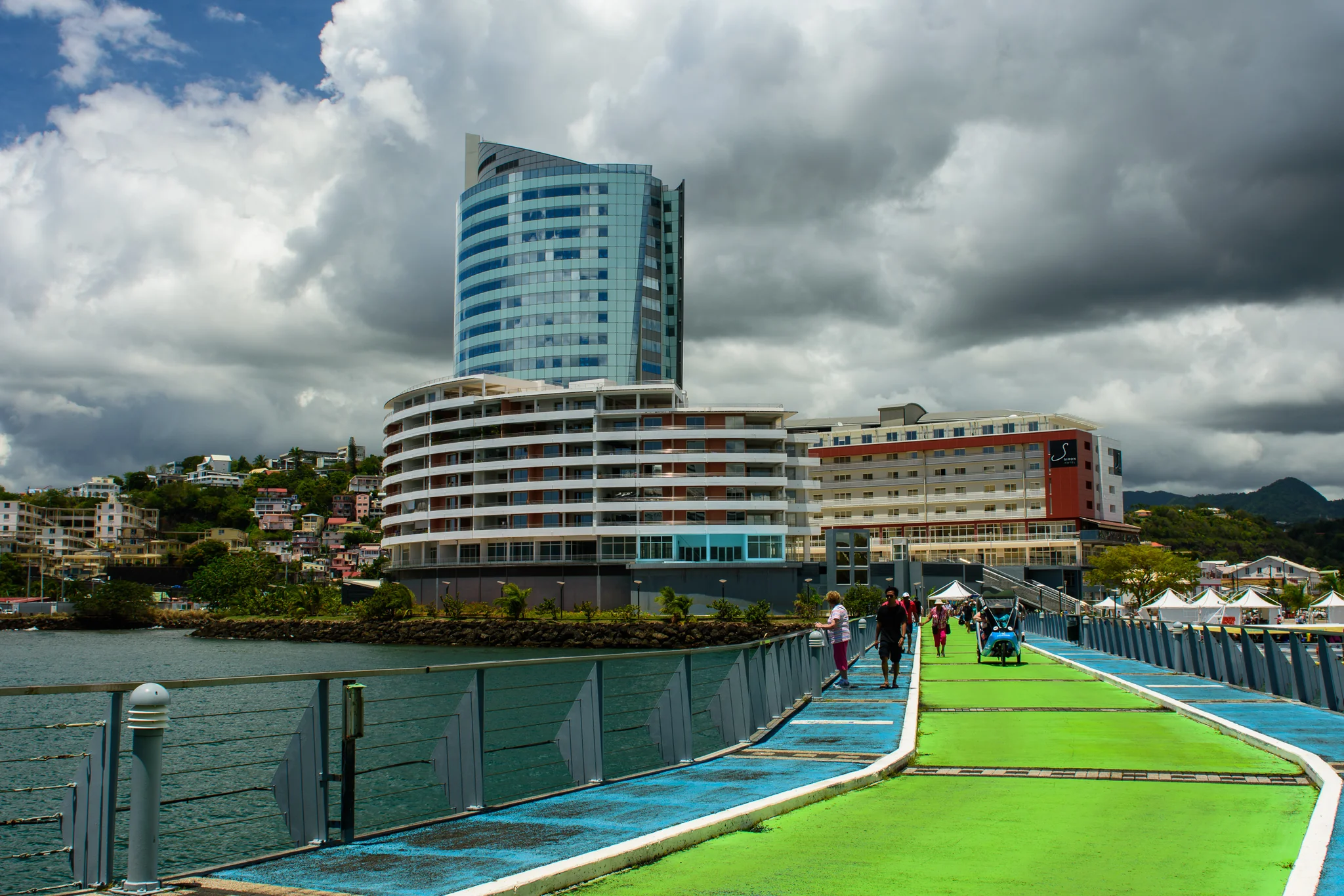 Modern waterfront complex and people on a pier beneath dramatic storm clouds