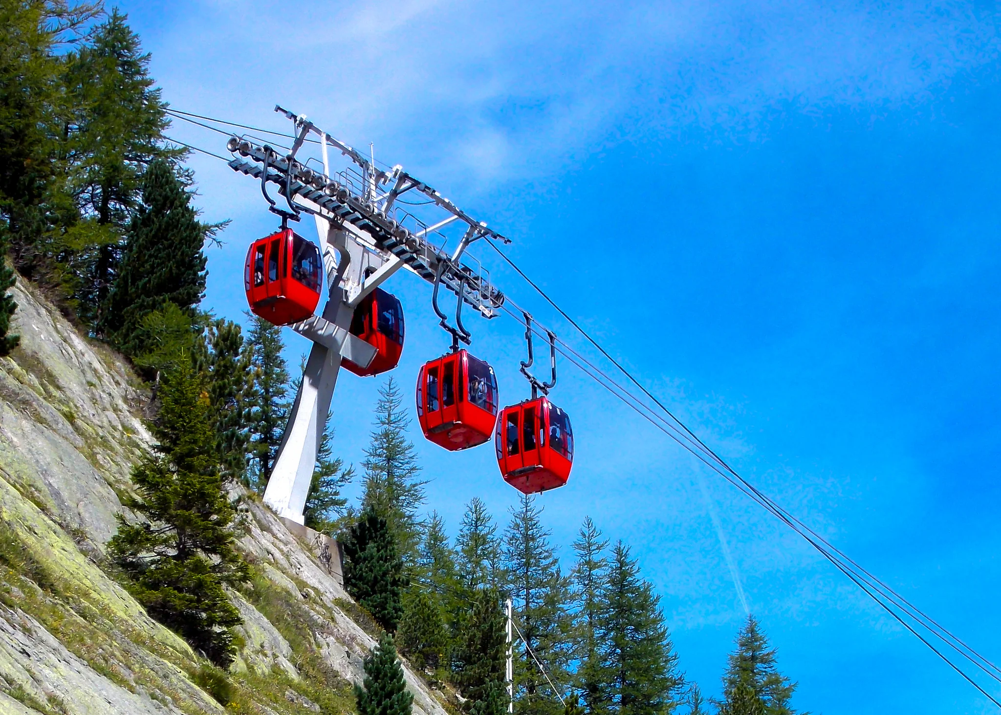 Red mountain cable cars crossing above alpine forest and rock