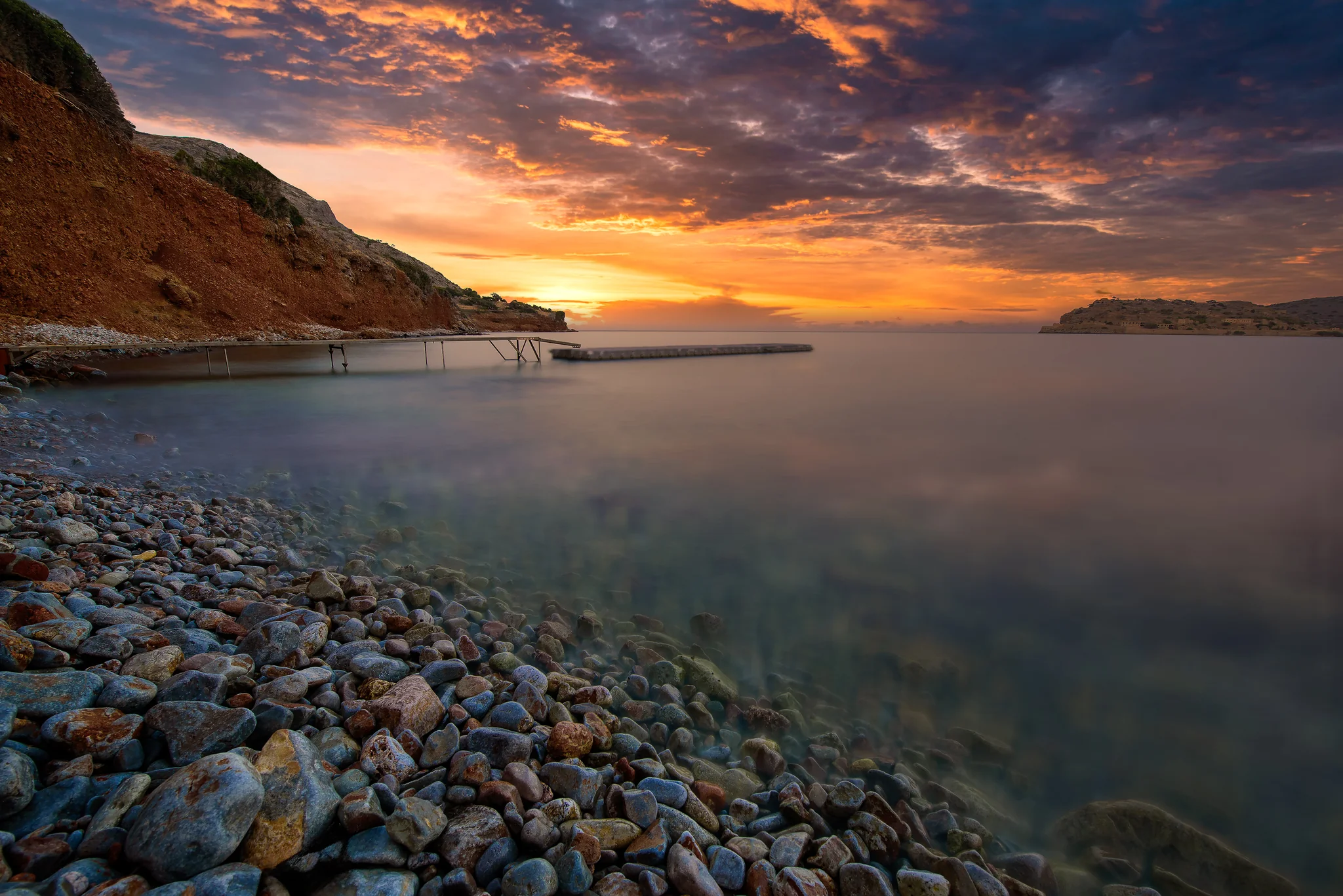 Rocky coastal cove with small piers beneath a fiery sunset sky